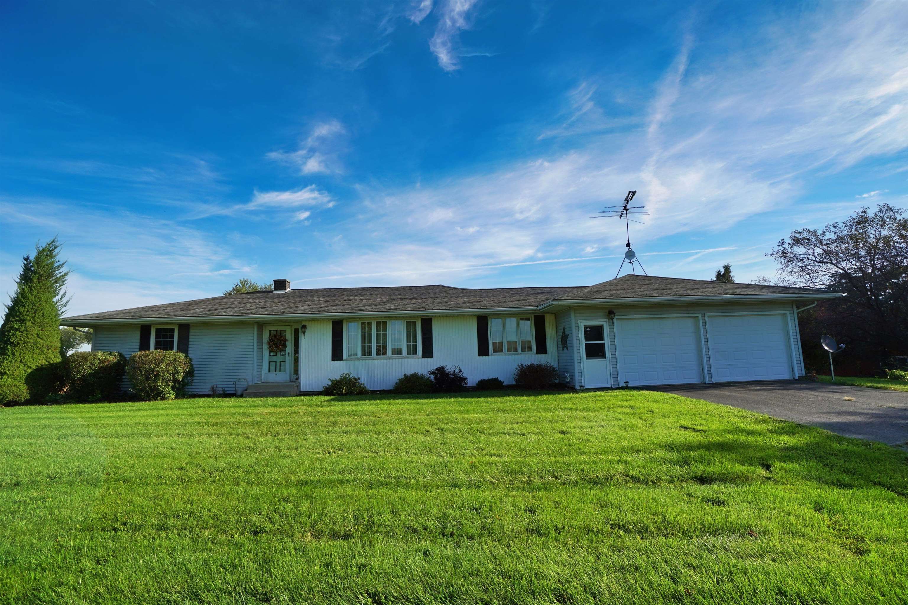 White single-story ranch house with attached two-car garage, rooftop antenna, and broad green lawn.