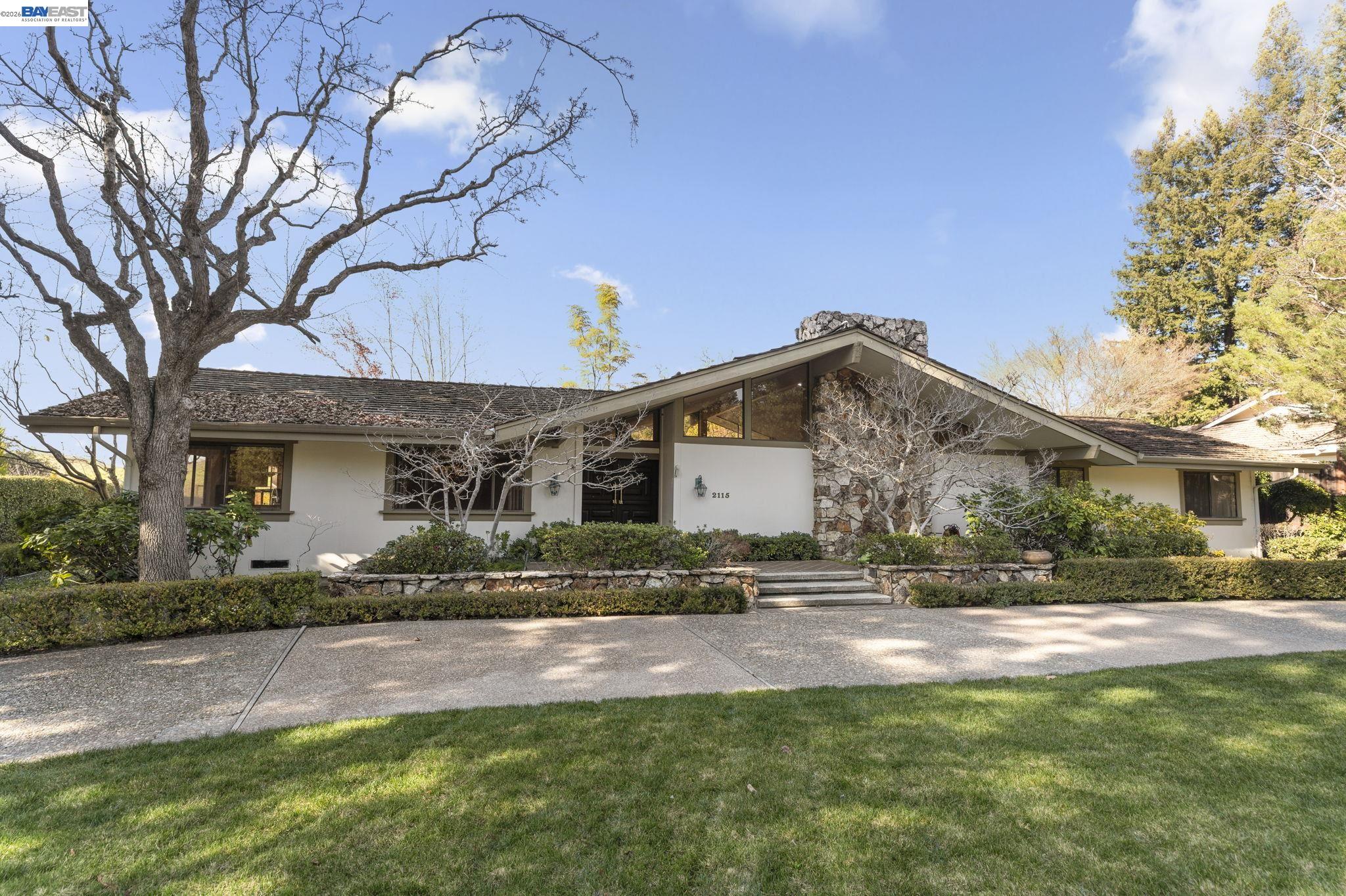 Single-story home with a stone entry surround, front steps, and mature trees.