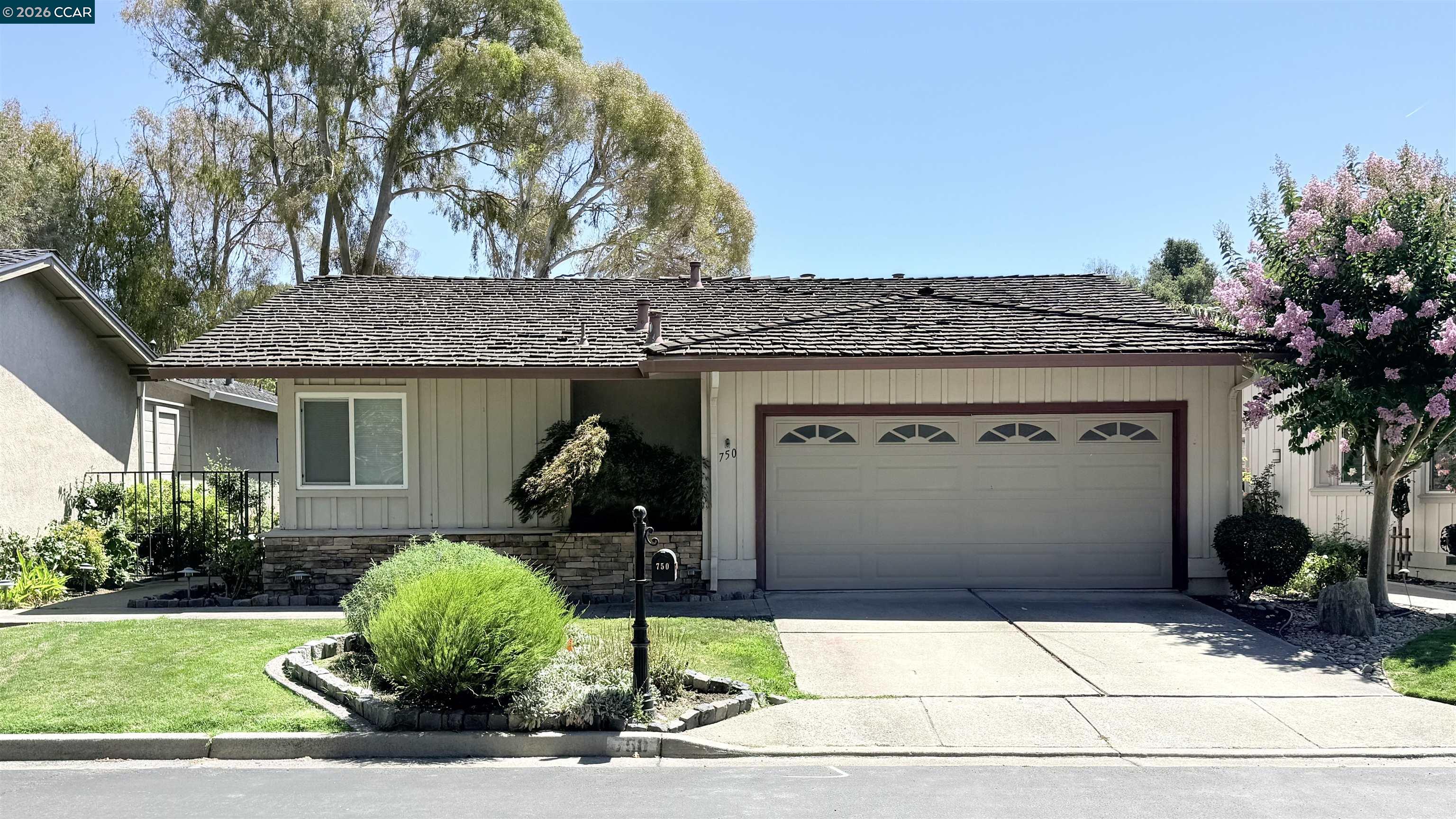 Single-story home with a two-car garage, landscaped front yard, and pink-flowering tree.