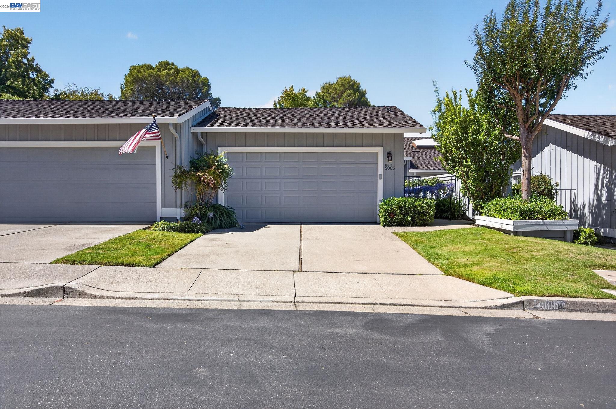 Gray suburban home with white garage doors, landscaped front yard, and an American flag.