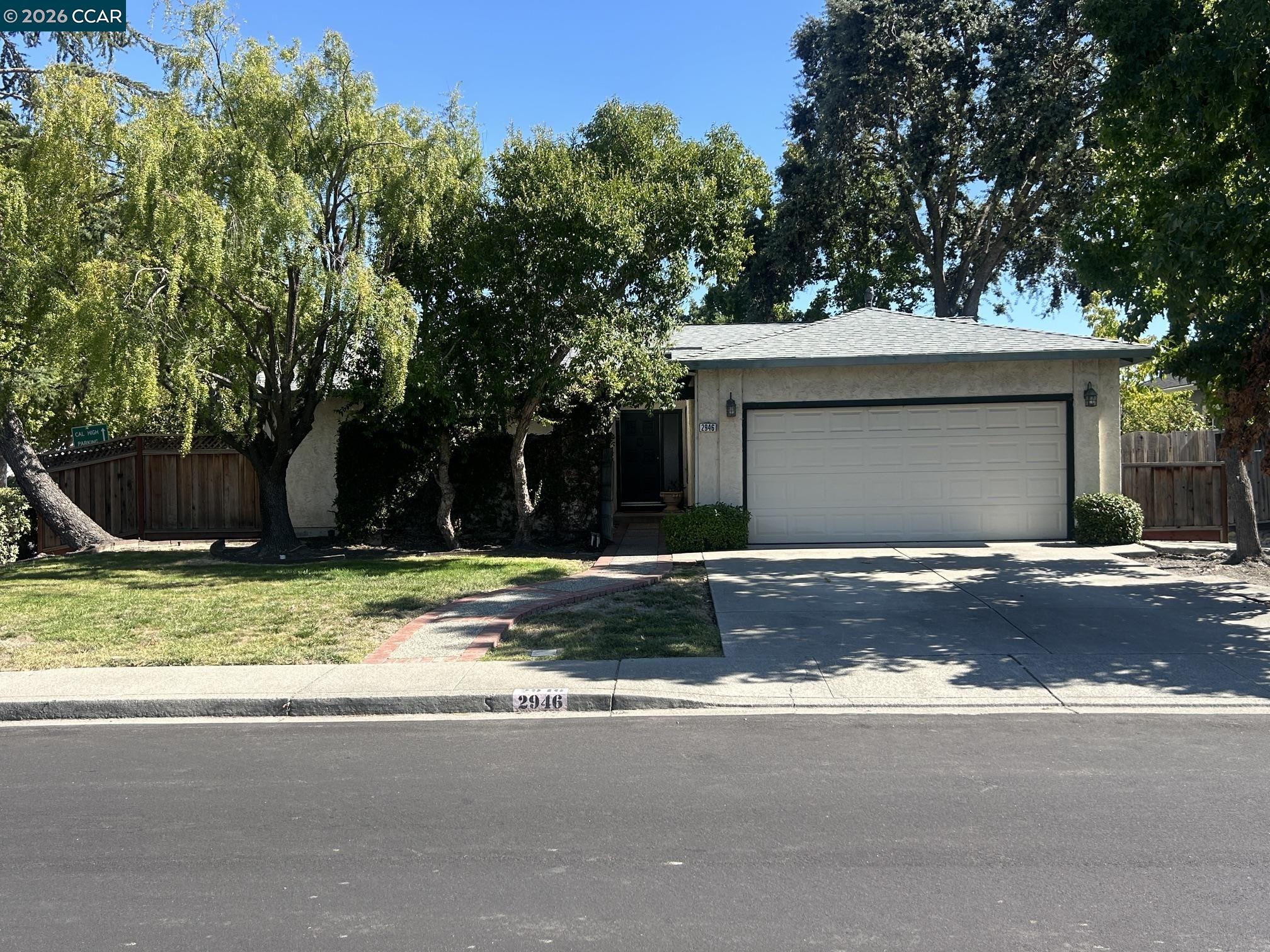 Single-story stucco home with a two-car garage, shaded by mature trees.