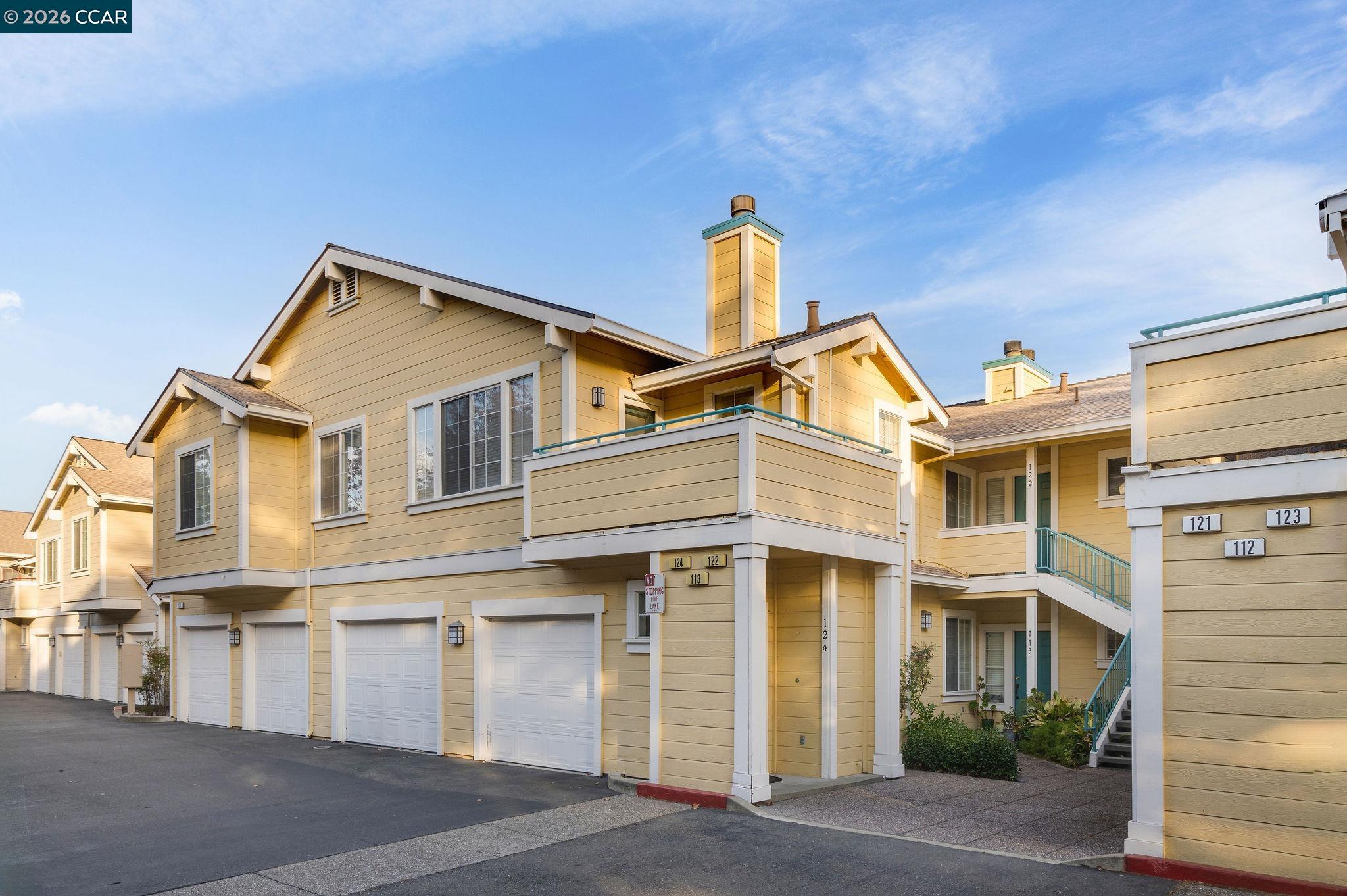 Tan multi-unit homes with garages and balconies, photographed in warm sunlight.