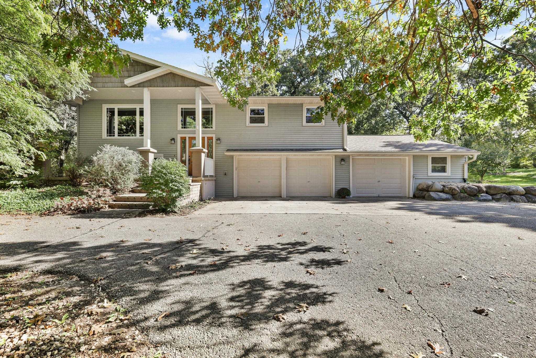 Gray two-story home with a three-car garage and landscaped entry beneath mature autumn trees.