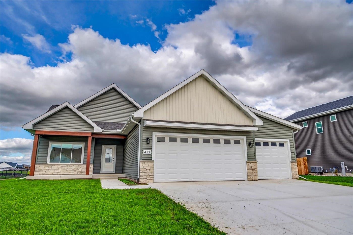 Gray-green suburban house with two white garage doors, stone accents, and a broad driveway.