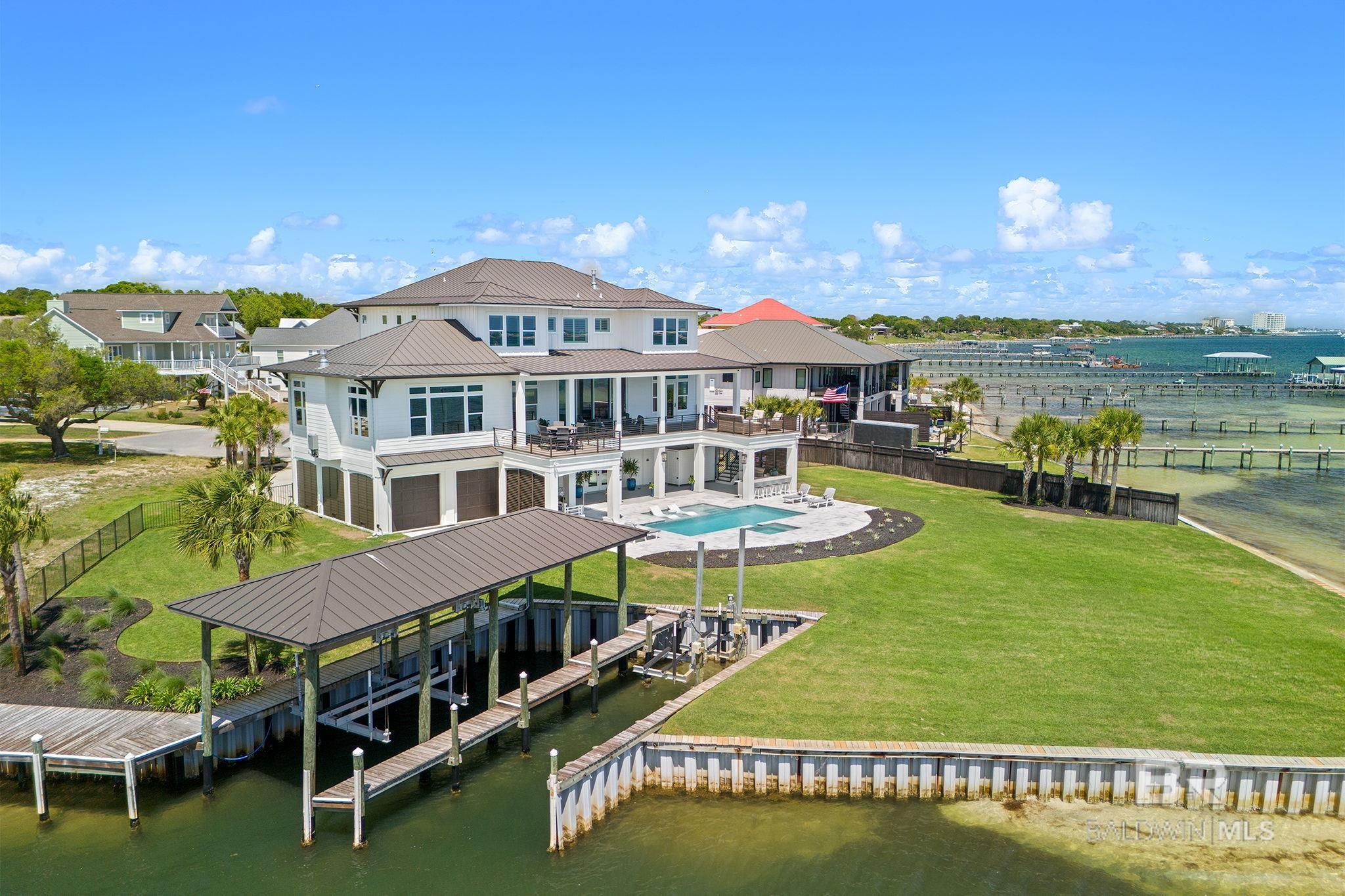 Experience luxury coastal living at its finest in this breathtaking 5-bedroom, 5 bath estate perfectly positioned on a ½-acre cul-de-sac lot with 217 feet of pristine waterfront on the Intracoastal Waterway and a private boat basin. Enjoy panoramic views of the Intracoastal and the Gulf, where gorgeous sunrises and stunning sunsets fill the sky each day—and watch the Blue Angels fly from the comfort of your own backyard. A boater’s paradise, this property offers direct access to the Intracoastal Waterway and is in close proximity to the Pass, providing effortless access to the Gulf of America or fishing, cruising, and coastal adventures. Inside, the home showcases white oak hardwood floors throughout, beautiful moldings, luxury marble and tile bathrooms, and a gourmet kitchen adorned with quartz countertops and backsplash, black stainless designer appliances, a Wolf built-in coffee system, and a butler’s pantry featuring custom cabinetry and walnut counters. The Bar & Game Room exudes a stylish speakeasy vibe, featuring a gas fireplace, walnut bar, beverage refrigerator, Scotsman ice maker, and beverage dispenser—a perfect gathering place for friends and family. Step outdoors to your private resort-style retreat with a Gunite heated pool and spa, surrounded by marble decking, and an outdoor kitchen equipped with a Blaze gas grill, Large Green Egg, beverage fridge, prep sink, and a full outdoor bathroom for added convenience. Additional highlights include a whole-house gas generator, an elevator servicing all three floors, and en-suite bedrooms finished with quartz, marble, and designer tile. Celebrated for its exceptional design and craftsmanship, this home has been featured in multiple luxury coastal magazines—a true testament to its architectural distinction and timeless beauty. This extraordinary waterfront residence seamlessly blends modern sophistication, comfort, and the ultimate coastal lifestyle.   Buyer to verify all information during due diligence.