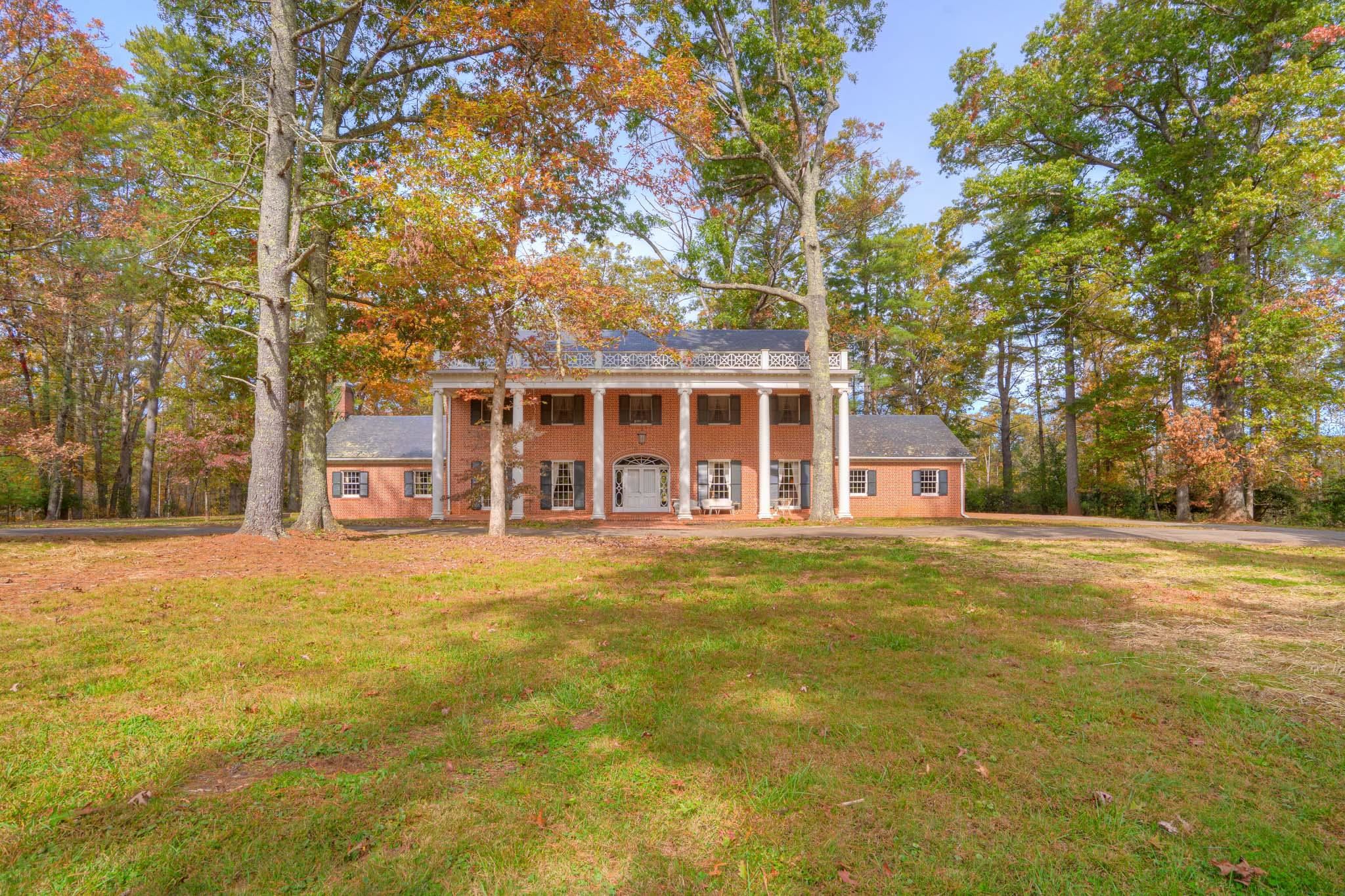 Classic Southern Colonial in the Heart of Floyd, timeless brick masterpiece that exudes elegance, craftsmanship, & Southern charm w/ 22+ acres fronting on 2 state roads w/ large pond. Nestled among mature hardwoods, minutes from downtown Floyd, this stately home offers the sophistication of a bygone era w/ comfort & warmth of classic design. Step into impressive Grand Foyer highlighted by sweeping, floating curved staircase, crystal chandelier, & intricate trim detailing. Main level features gracious Formal Living Room & Formal Dining Room adorned w/ rich HW flooring, ornate dental crown molding & large arched doorways that invite easy flow & natural light. Upstairs, spacious bedrooms showcase original millwork & elegant touches. The stately, 2-story, front columns & grand portico to welcoming porch & landscaped grounds, this home's unmatched character offers rare opportunity to own remarkable piece of architectural heritage. Ideal as a private residence, event venue, or boutique inn.
