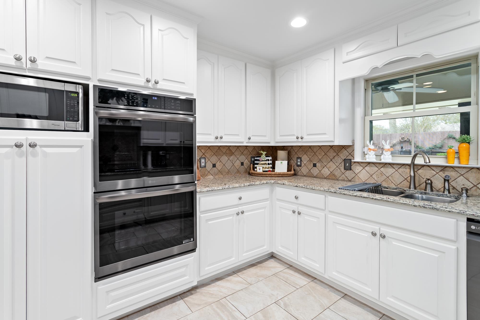 Kitchen corner showing built-in double oven, microwave, white cabinets, and granite counters