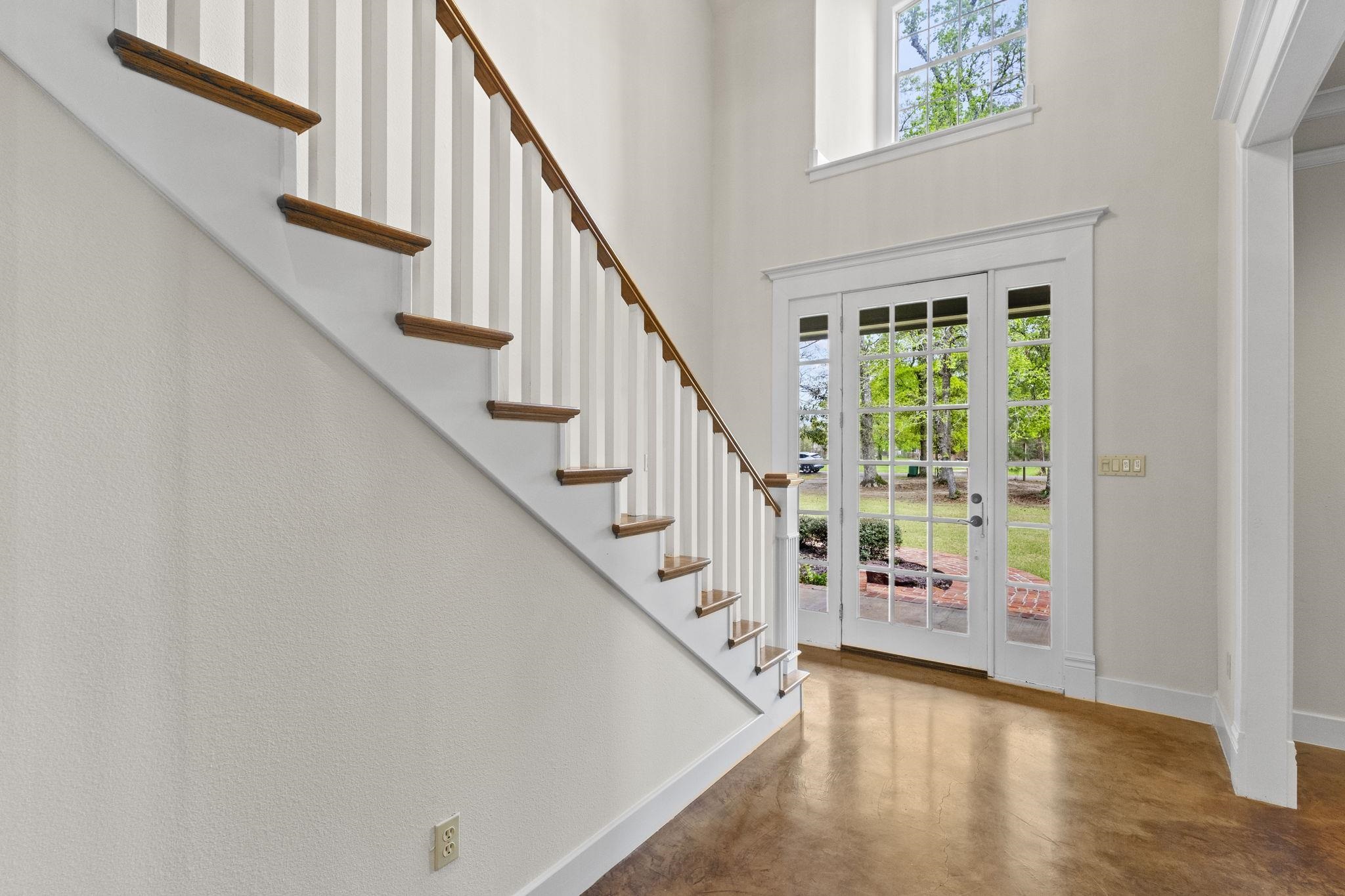 Entry foyer with polished concrete floors, white staircase with wood treads, and French doors leading to outdoor spaces