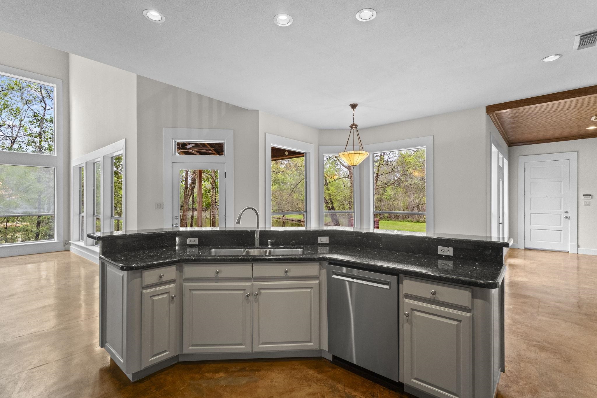 Kitchen island with sink, black granite countertops, and panoramic windows overlooking wooded area
