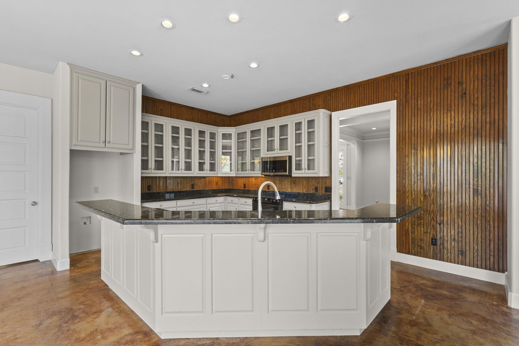Kitchen featuring extensive glass-front cabinets, wood backsplash, and large island with granite countertops