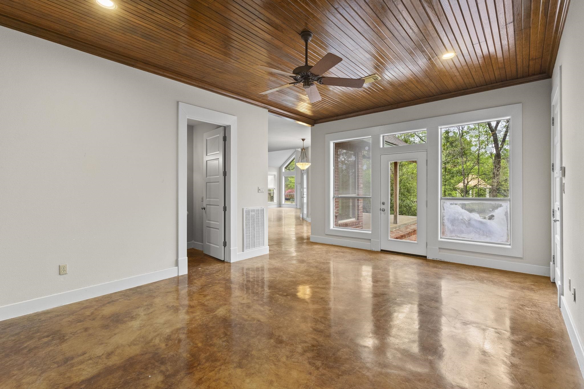 Spacious living room with wood plank ceiling, ceiling fan, stained concrete floors, and French doors leading to outdoor space