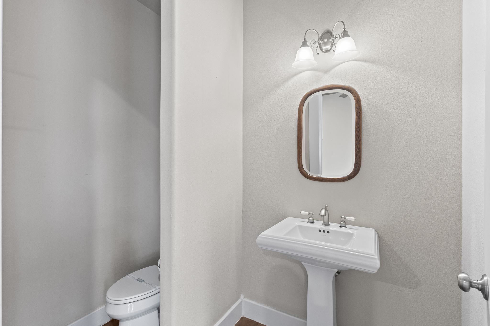 Half bath with pedestal sink, oval mirror with wood frame, and vanity lighting
