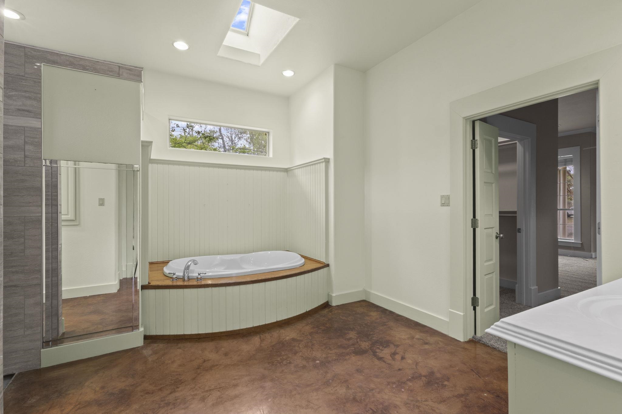 Primary bathroom with corner soaking tub, skylight, wood surround, and glass shower enclosure
