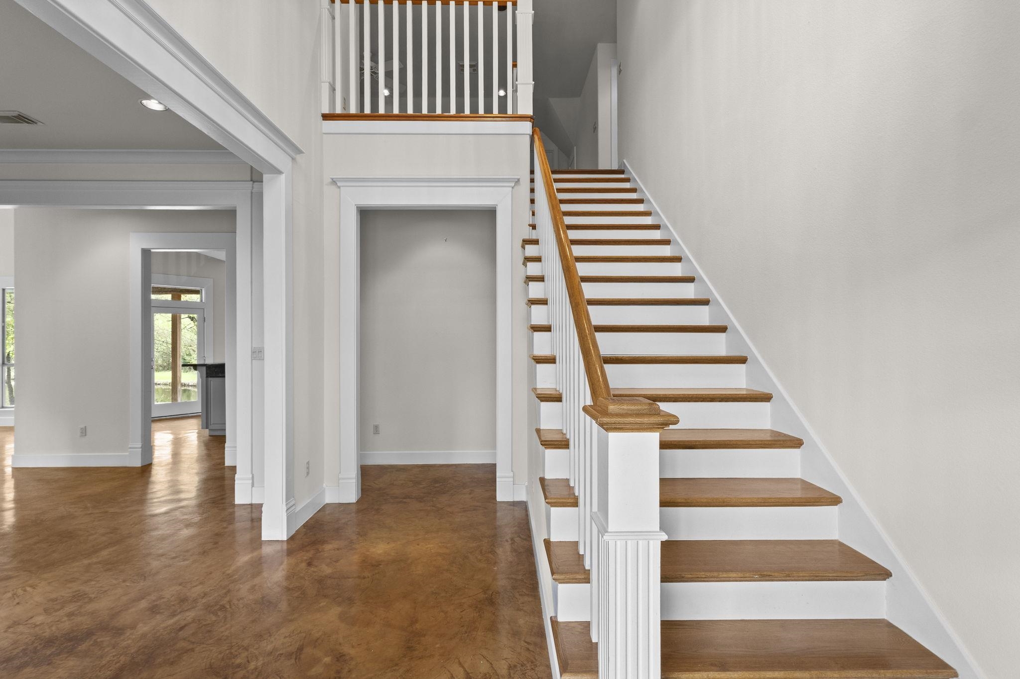Main staircase with white painted balusters, wood handrail and treads, showing open floor plan with polished concrete floors