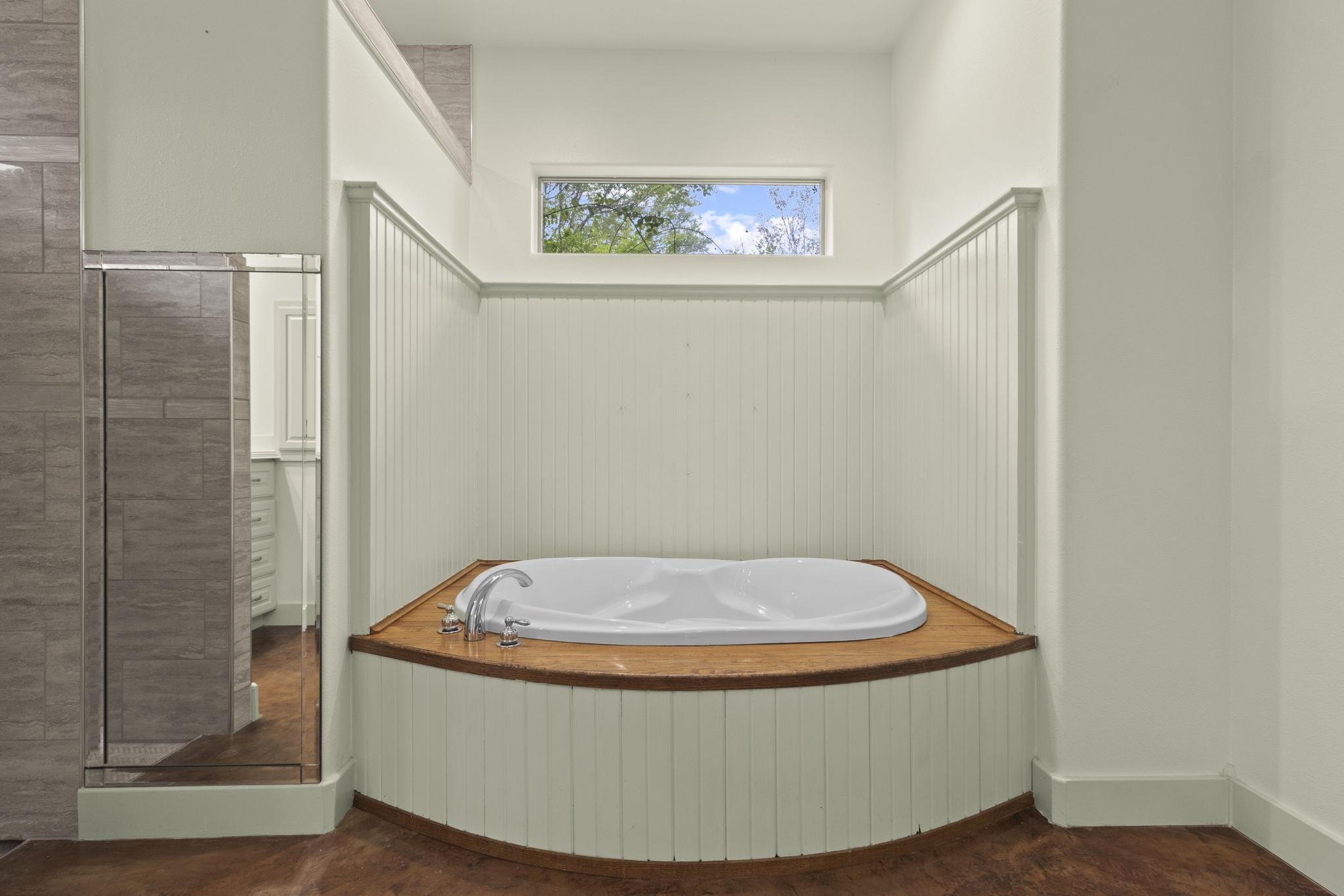 Corner soaking tub with wood trim, white beadboard wainscoting, and window with natural light