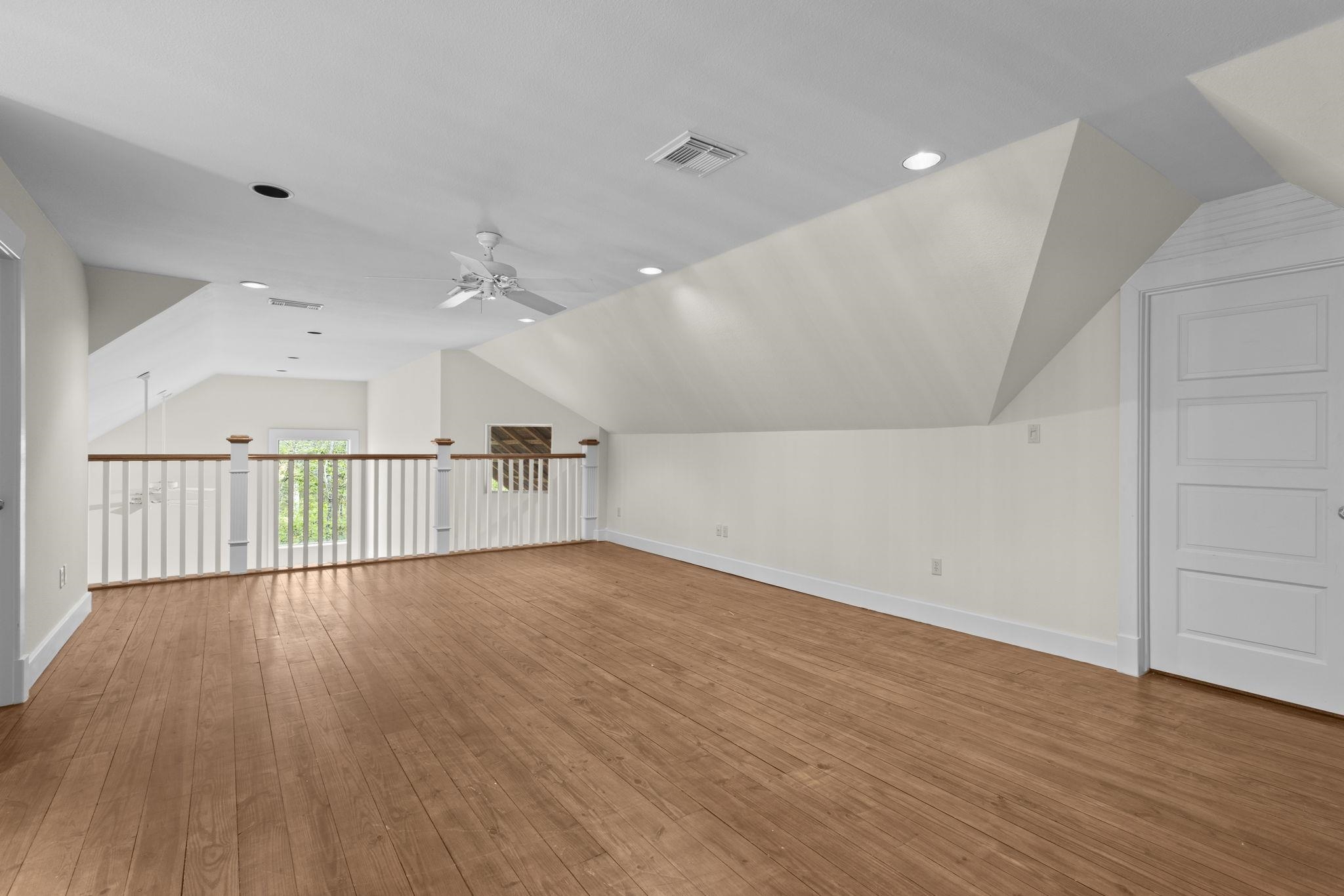 Upper level loft space with vaulted ceiling, white railings, hardwood floors, and built-in storage