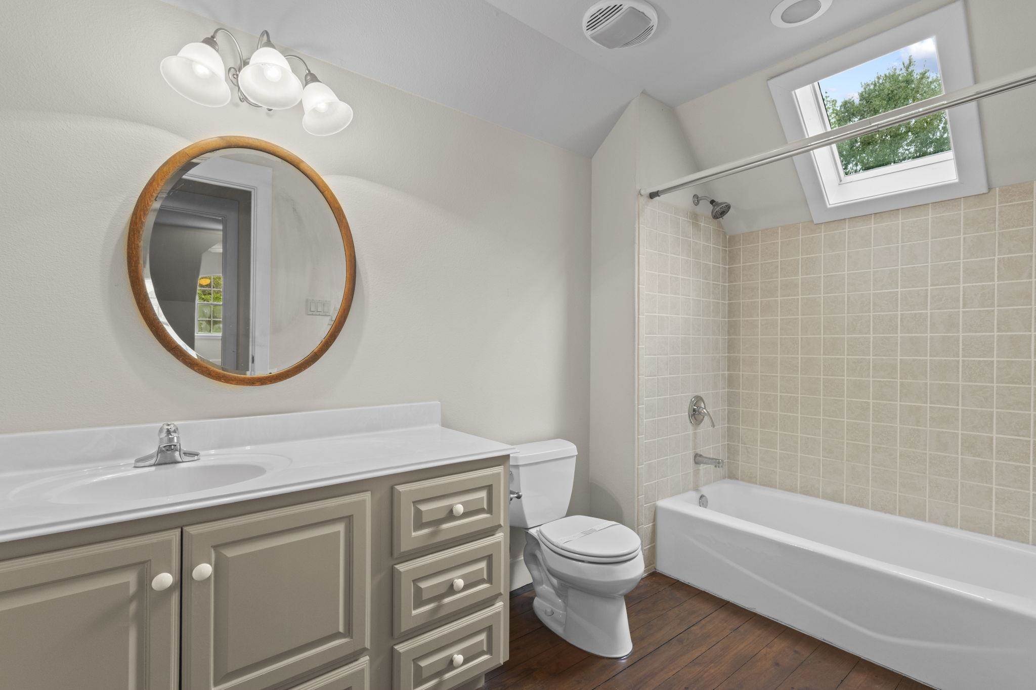 Full bathroom with vanity, round mirror, tub/shower combo, and tiled walls