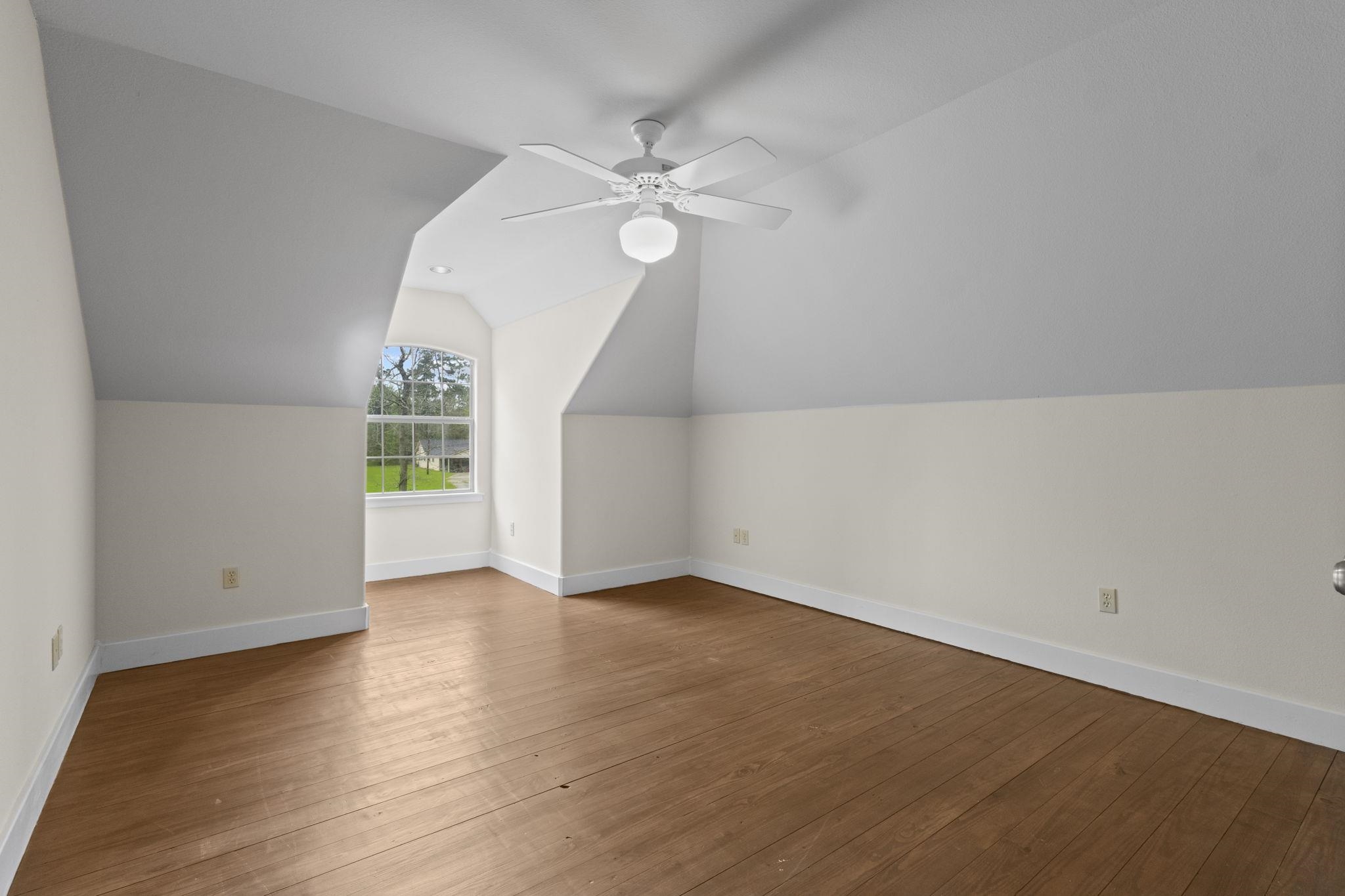 Bedroom with slanted ceiling, hardwood floors, arched window, and ceiling fan