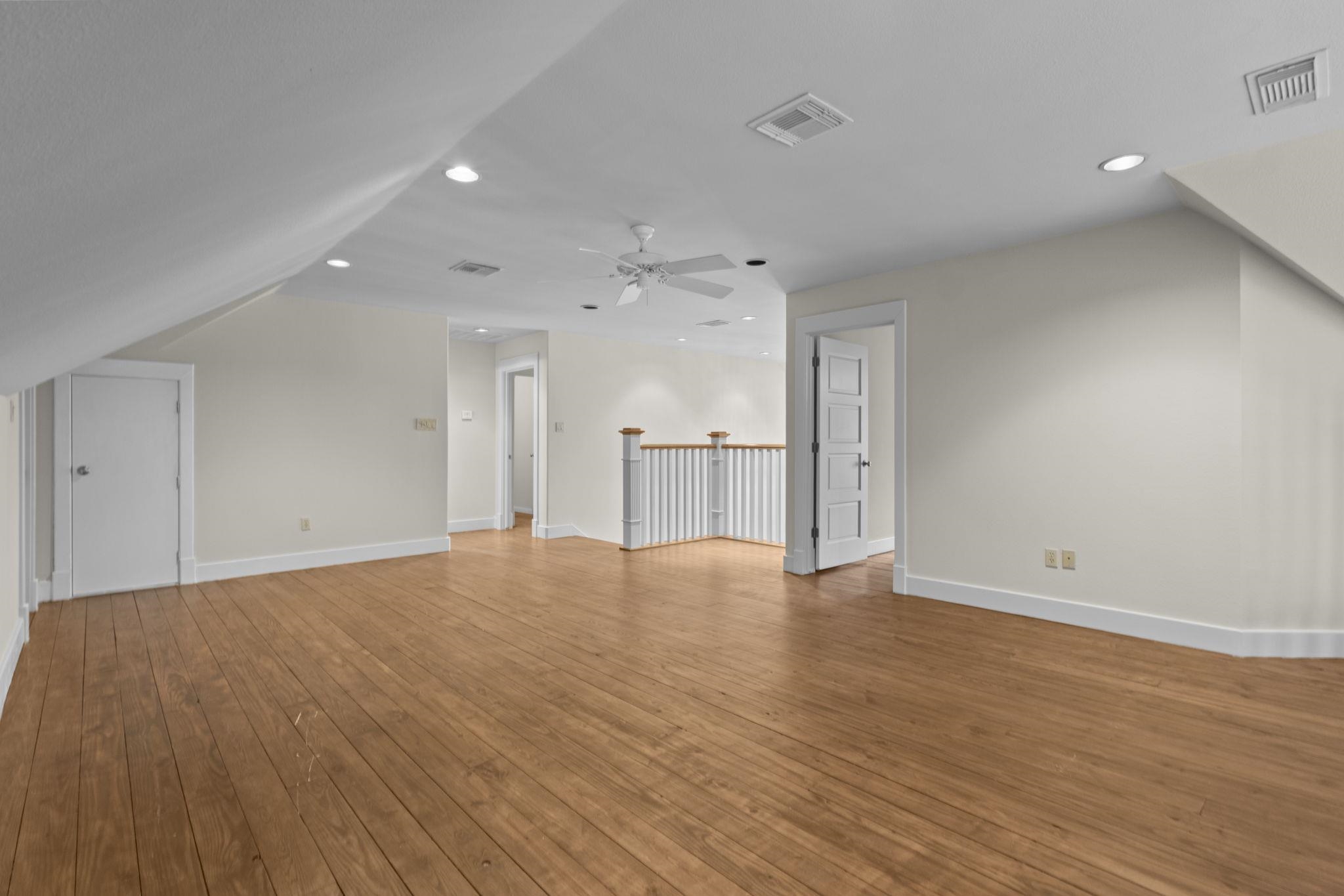 Large open living space with hardwood floors, vaulted ceiling, recessed lighting, and stair railing