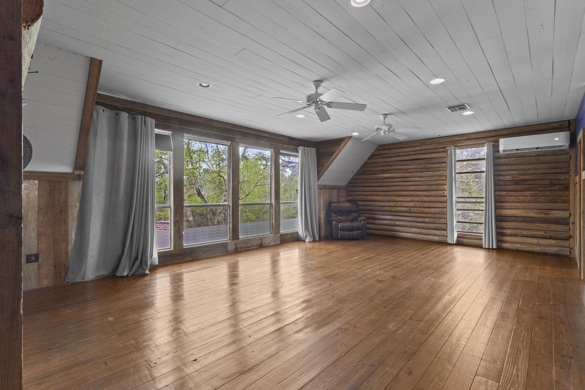 Large recreation room with log walls, hardwood floors, white plank ceiling, and ceiling fans