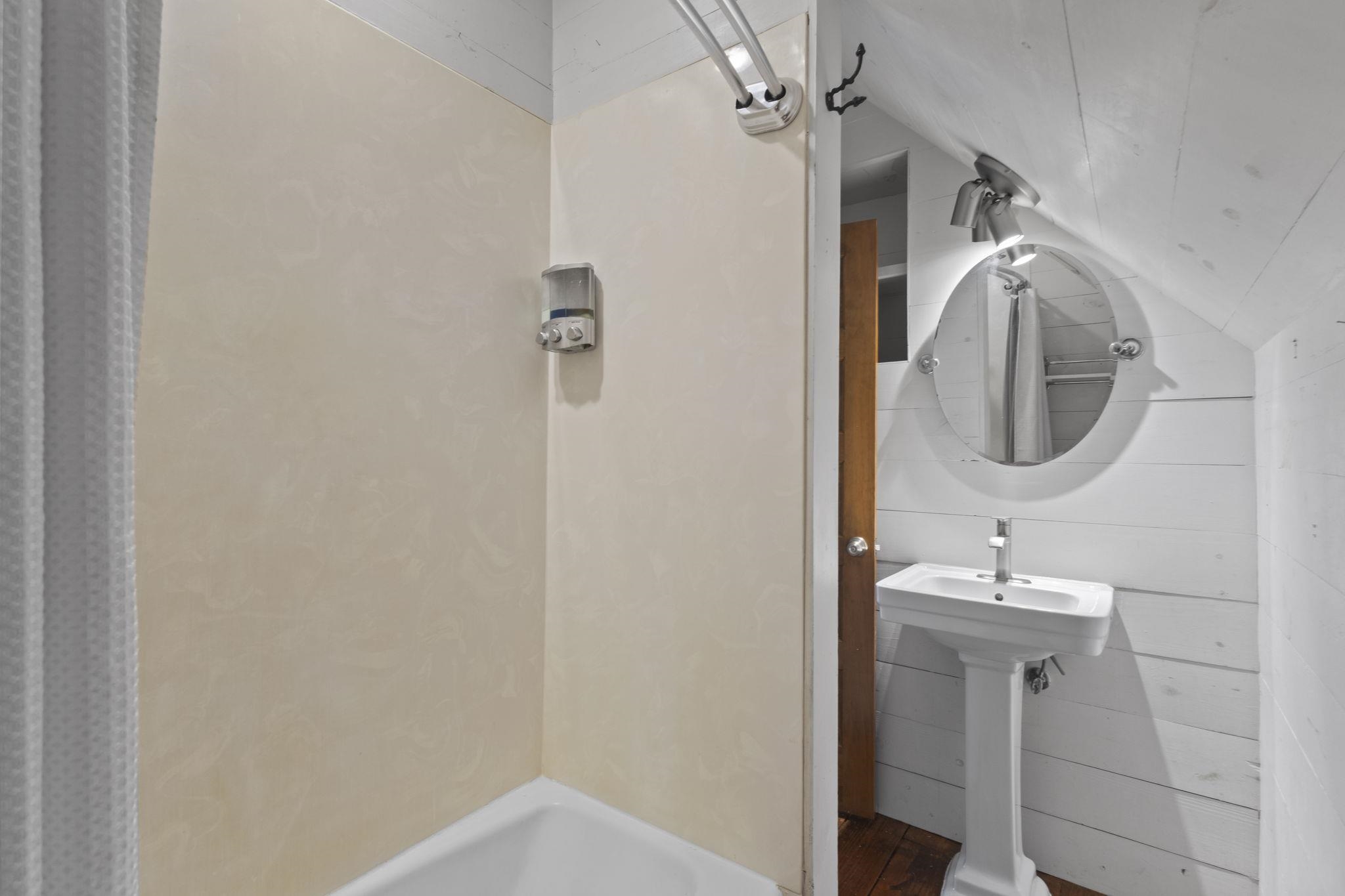 Modern bathroom with white pedestal sink, round mirror, and shower area