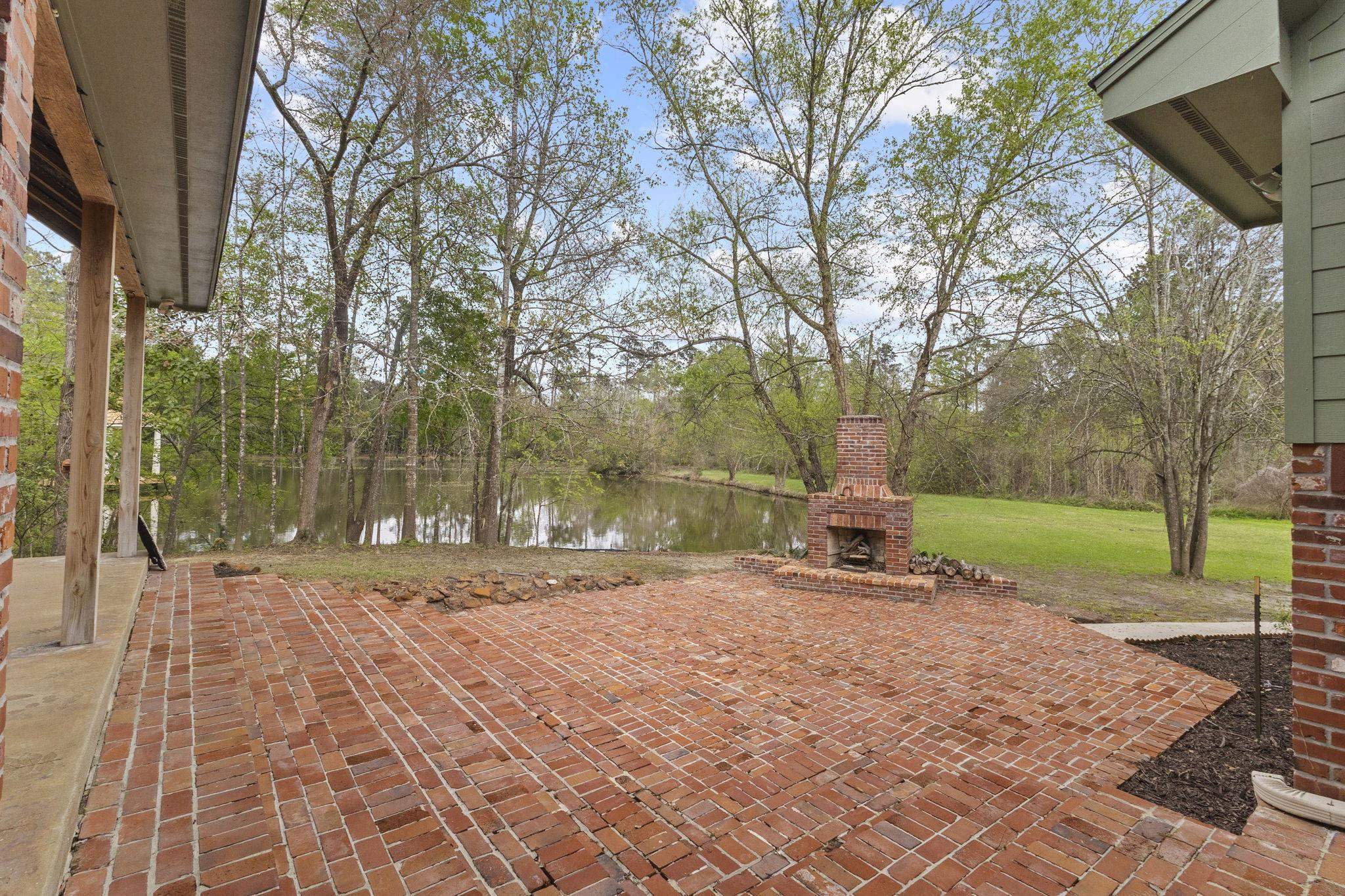 Brick patio with outdoor fireplace and pond view in wooded setting