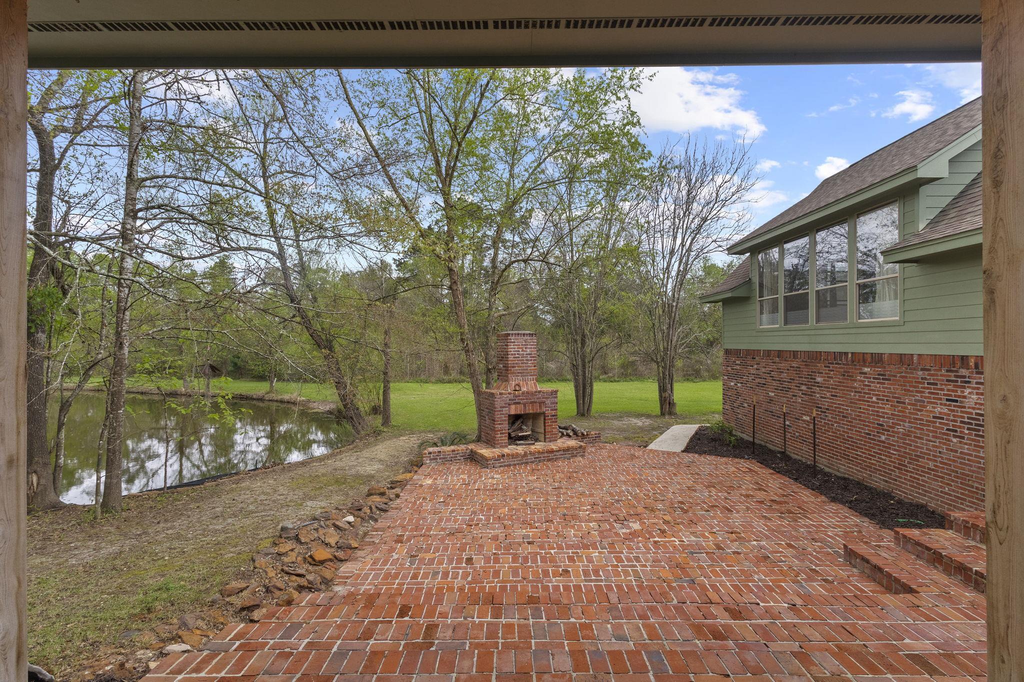 View from covered patio showing brick outdoor fireplace and pond beyond