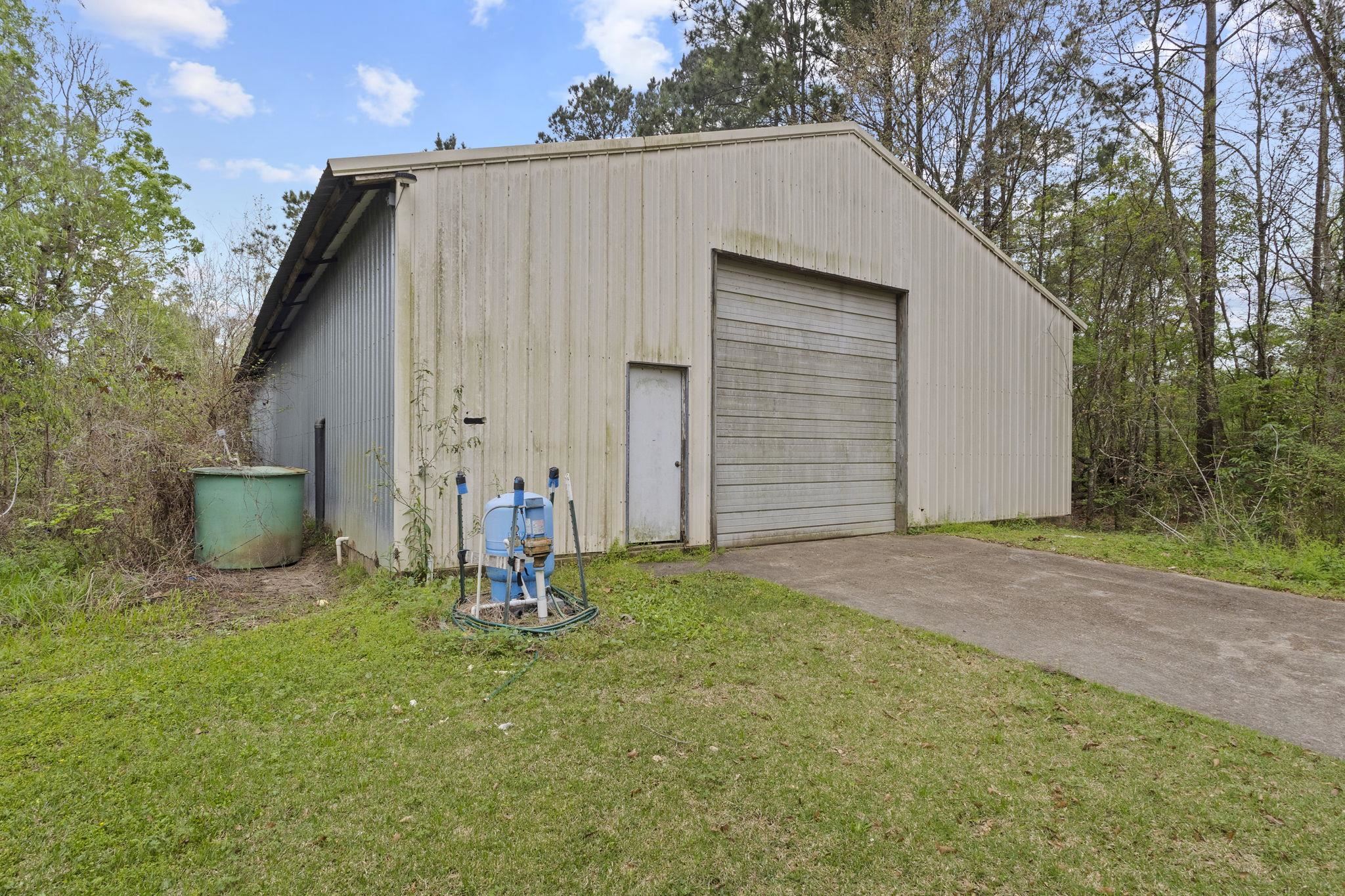 Metal workshop building with roll-up door and water well system in wooded setting