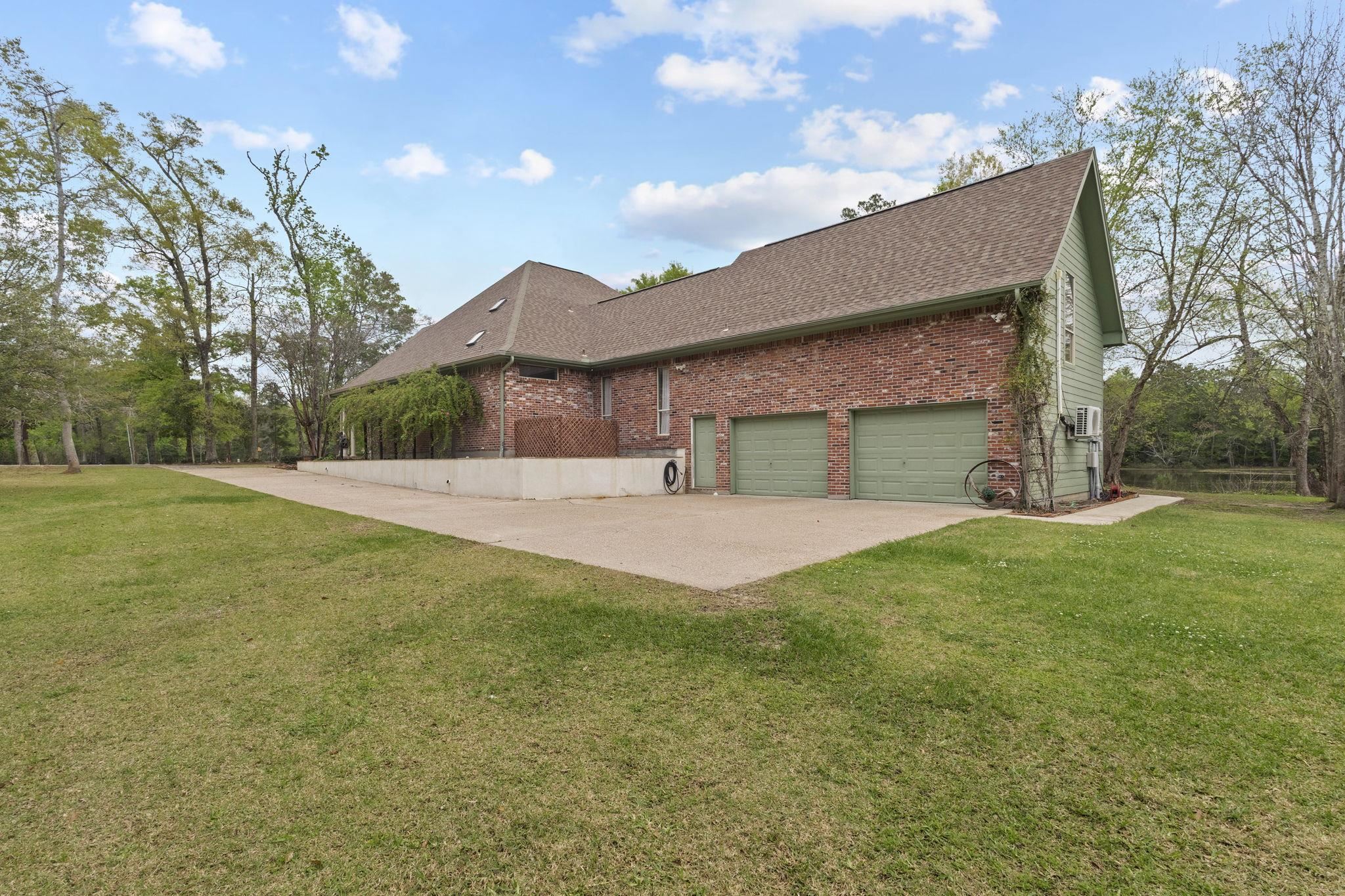 Brick and siding home with attached garage surrounded by mature trees and large lawn