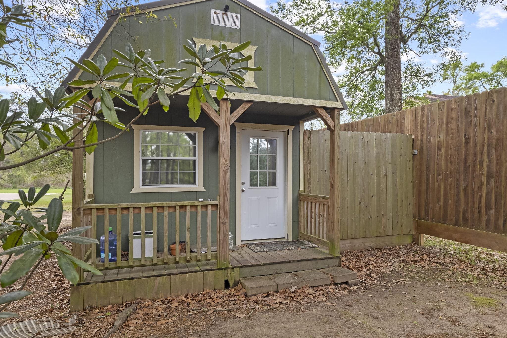 Small green cabin-style building with covered front porch and wooden fence