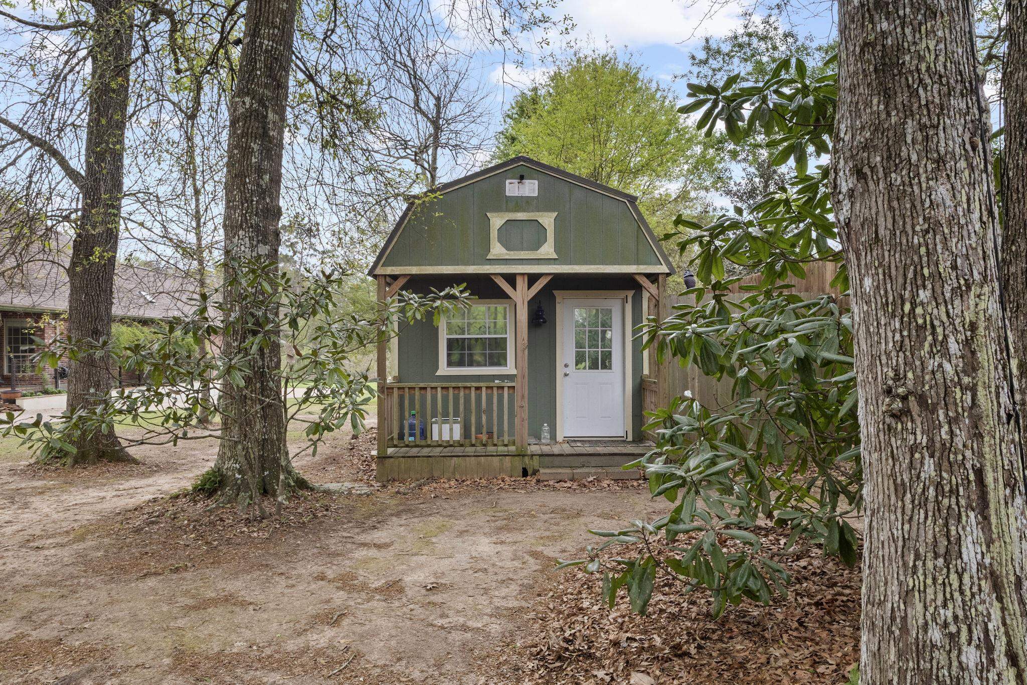 Green cabin building nestled among mature trees with wooden deck and railings