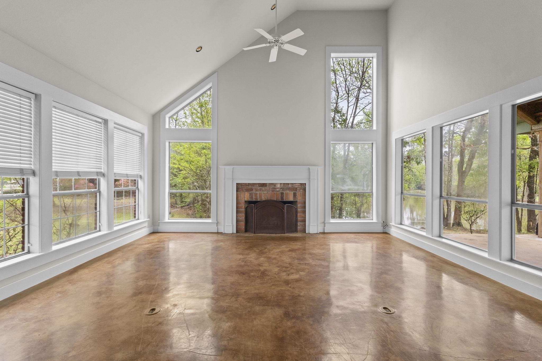 Great room with vaulted ceiling, brick fireplace, floor-to-ceiling windows, and polished concrete floors