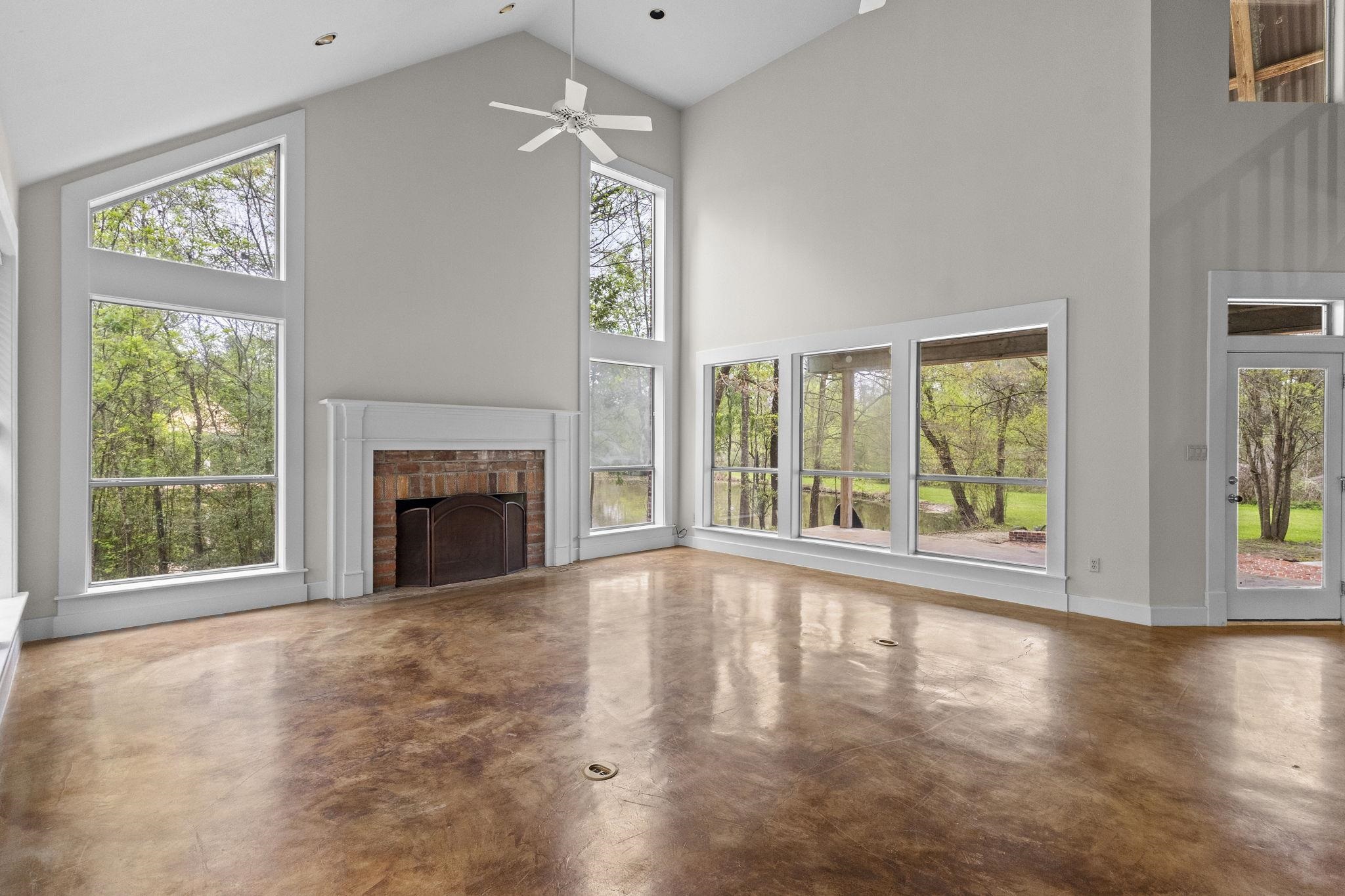 Spacious living room with vaulted ceilings, brick fireplace, large windows, and polished concrete floors