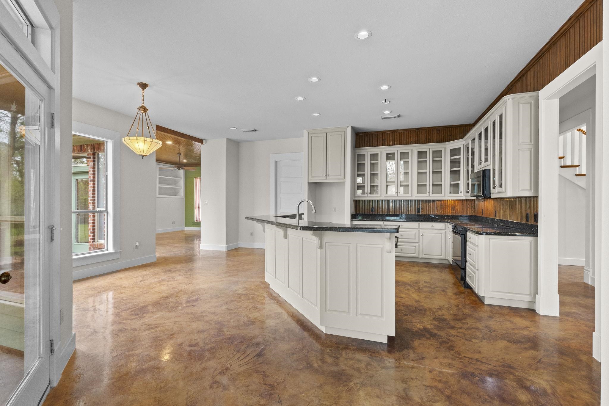 Open kitchen with white cabinets, black granite countertops, wood backsplash, and kitchen island