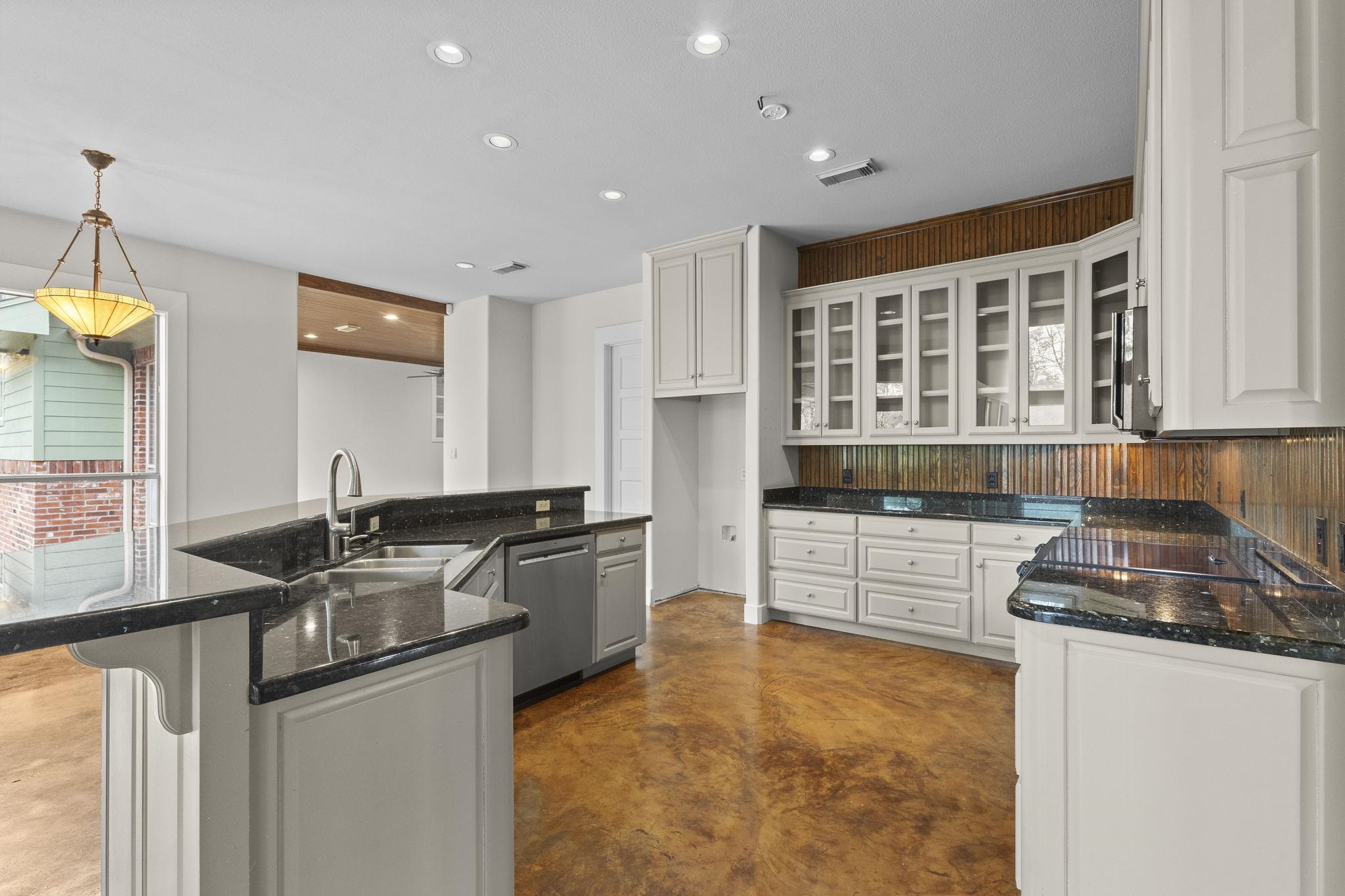 Kitchen view showing curved island, black granite countertops, and wood backsplash with glass-front cabinets