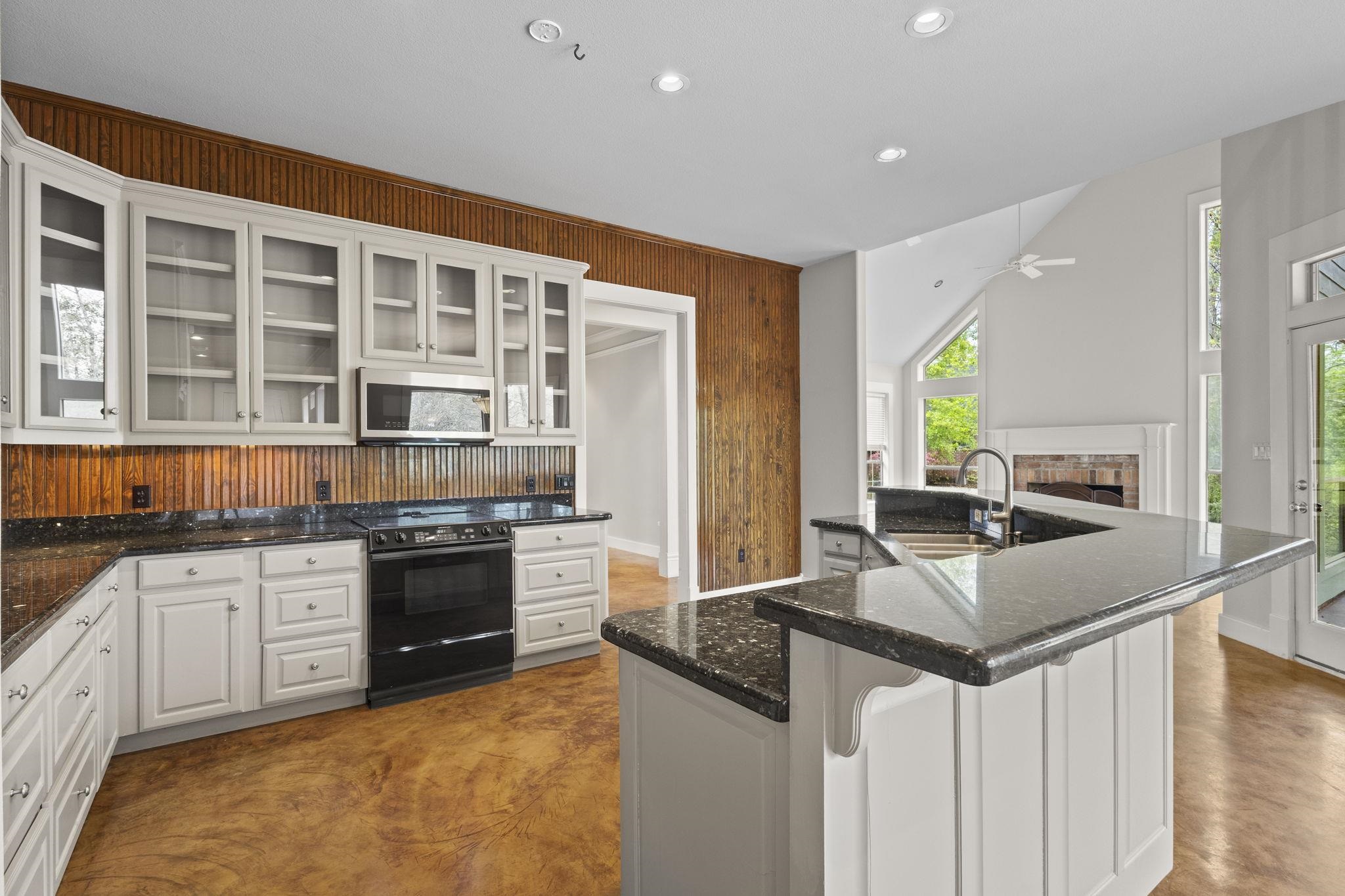 Kitchen showing range area with wood backsplash, white cabinets, and connection to living area