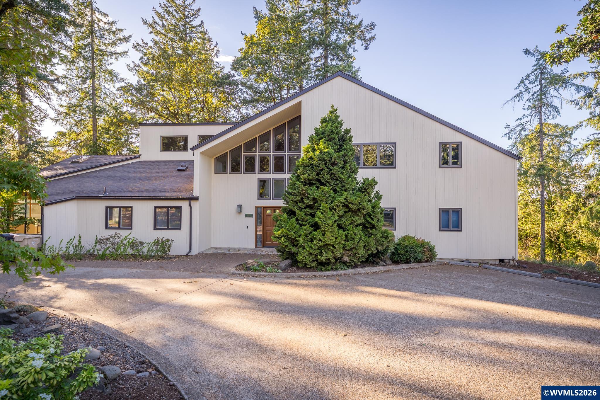 Set on 1.57 hilltop acres, this 5,800± sqft contemporary home frames sweeping valley views with walls of windows and soaring ceilings. 5BR/4.5BA, living room, formal dining room, family room w/fireplace, spacious kitchen w/sunroom and deck. Primary suite w/fireplace, balcony, walk-in closet on the main w/two more bedrooms and one bath, office w/storage. Upstairs are two bedroom suites, media room and loft. Downstairs is 2-car garage, bonus rm, sauna. New roof, new flooring throughout. Separate two-car shop. Welcome to a hilltop retreat where Oregon’s valley views take center stage. Set on 1.57 private acres with a circular driveway, this 5,800± square foot contemporary pairs dramatic architecture with true everyday comfort. A new roof and new flooring throughout.Step inside to a light-filled foyer and a living room framed by walls of windows beneath soaring, vaulted ceilings. The family room features a gas fireplace and huge windows made for soaking in the view. The warm wood kitchen, with granite counters, a tiled backsplash and a sunny breakfast nook, opens to a glass-roofed sun room and deck, perfect for morning coffee or evening gatherings. A formal dining room and a dedicated office complete the heart of the home.The main-level primary suite is a true retreat with its own gas fireplace, private bath and walk-in closet, plus deck access to the views. Two additional main-level bedrooms share a guest bath, making one-level living easy.Upstairs, a media room sets the stage for movie nights, and two bedroom suites each have a full bath, ideal for family, guests or multigenerational living. The lowest level is built for wellness and function, with a workout room, sauna and two-car garage.Outside, mature evergreens, Japanese maples and gardens surround the home, while a gently sloping lawn leads to peaceful pastoral views of rolling farmland. Golden-hour light pours through the trees, and every season brings a new show. A detached two-car shop adds even more room for projects, hobbies, equipment or storage.With five bedrooms, four and one-half baths and space for every purpose, this rare property offers privacy, beauty and the kind of setting you will not want to leave. Whether you are hosting a crowd or craving quiet, it all fits here. Homes with this much character, acreage and view rarely come along.