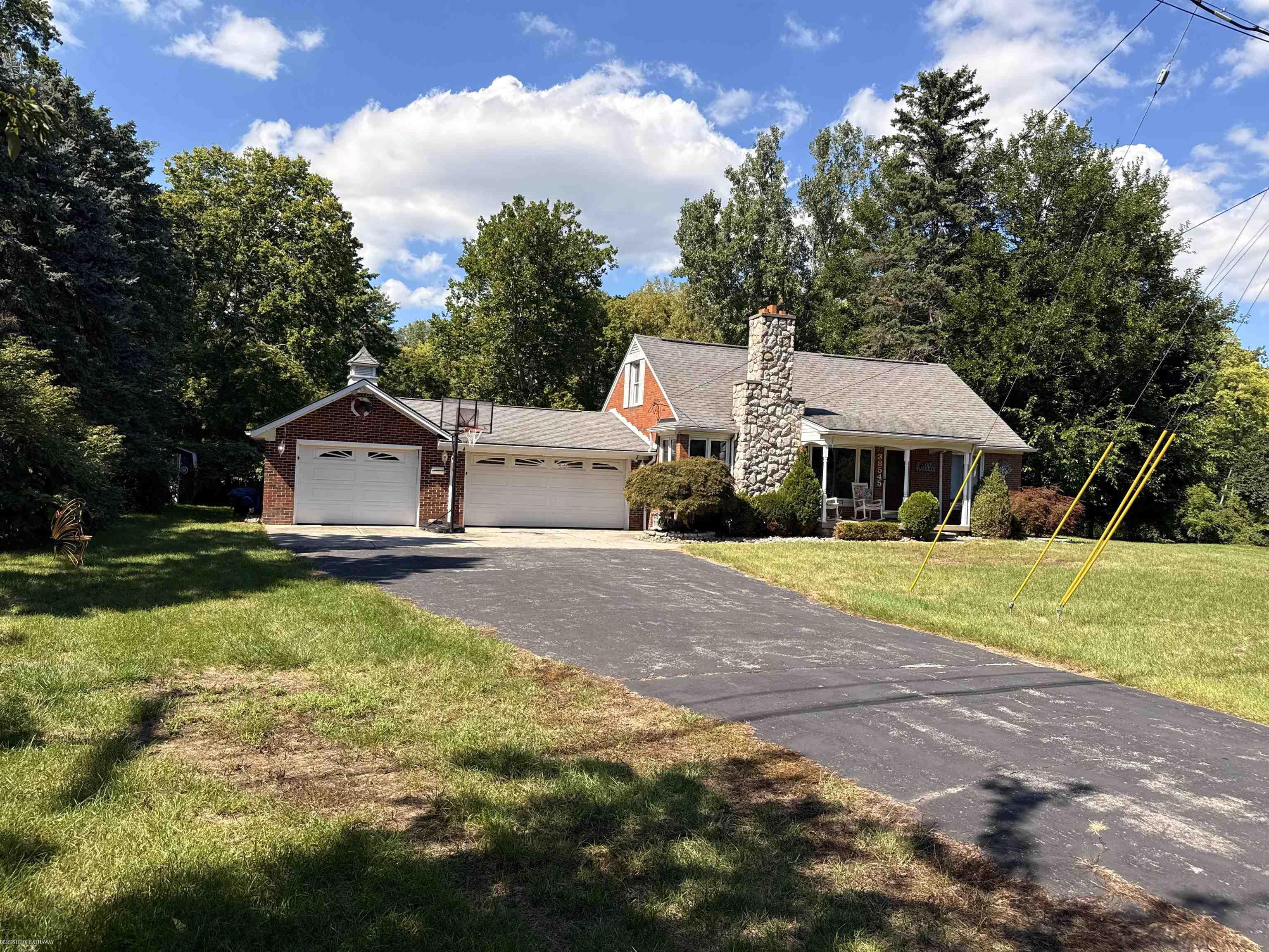 Suburban home with two garage doors and a tall stone chimney, surrounded by mature trees.