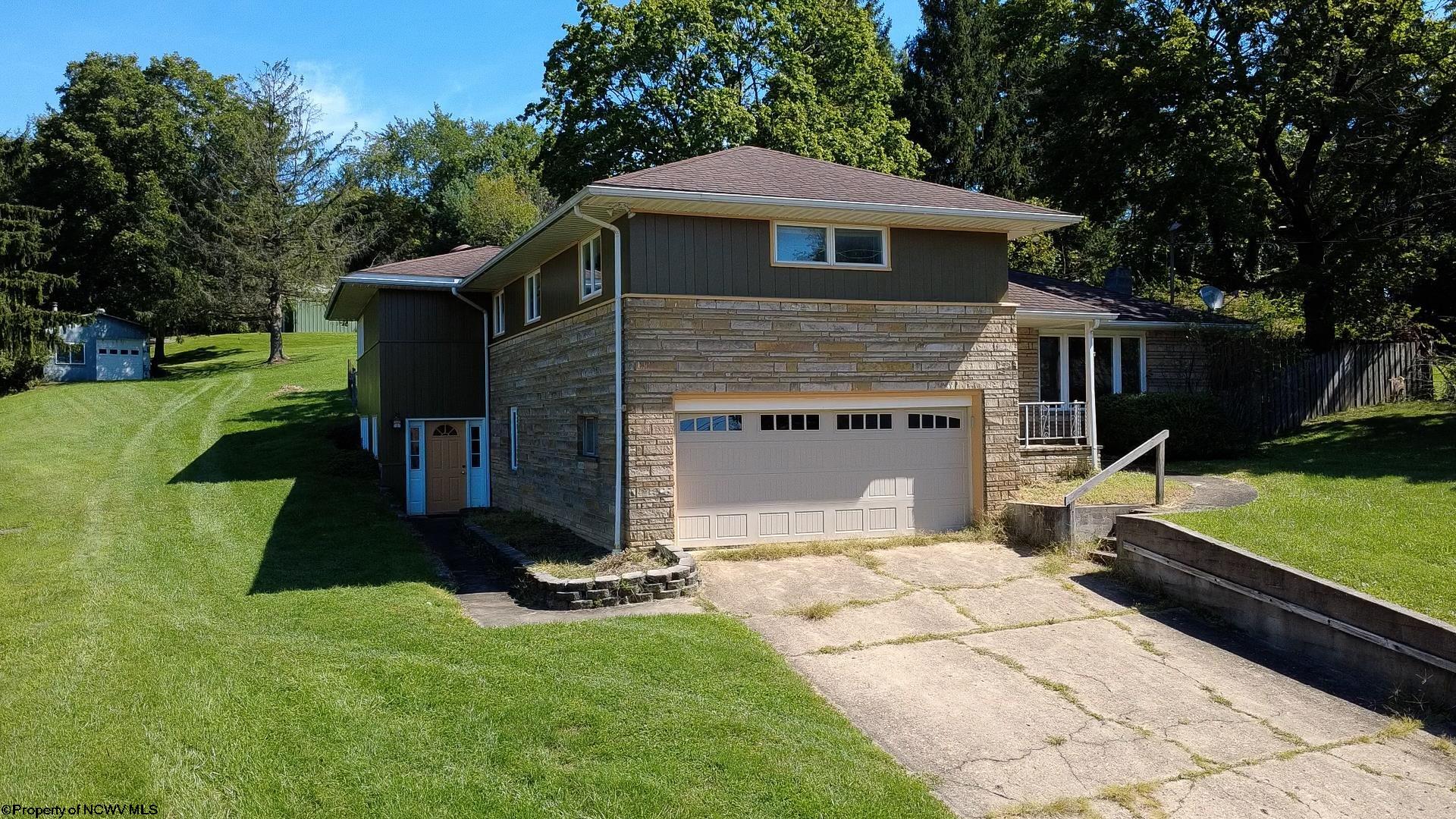 Split-level home with a stone facade, attached double garage, broad driveway, and mature trees.