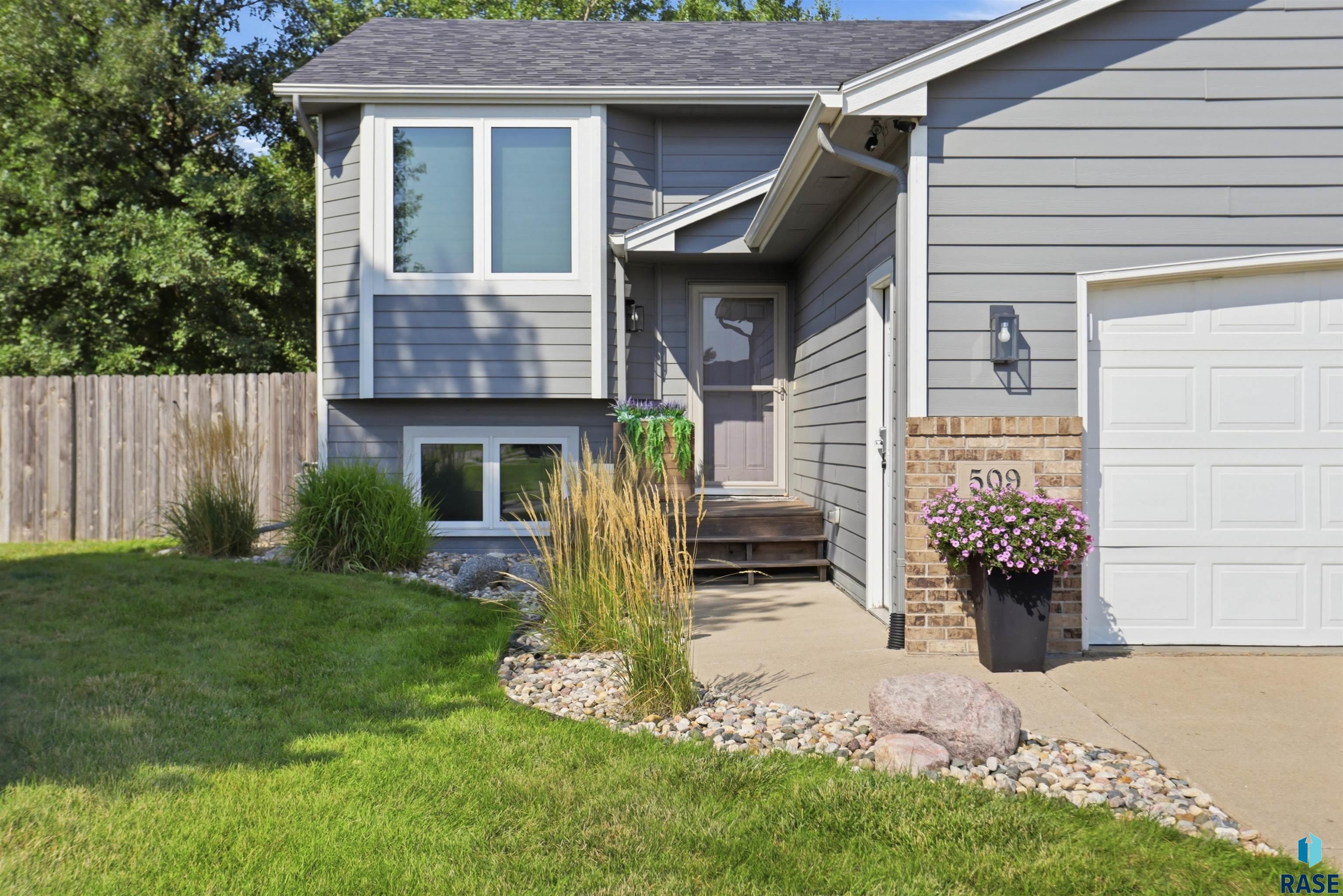 Gray split-level house with attached garage, landscaped front entry, and flower planter beside address 509.