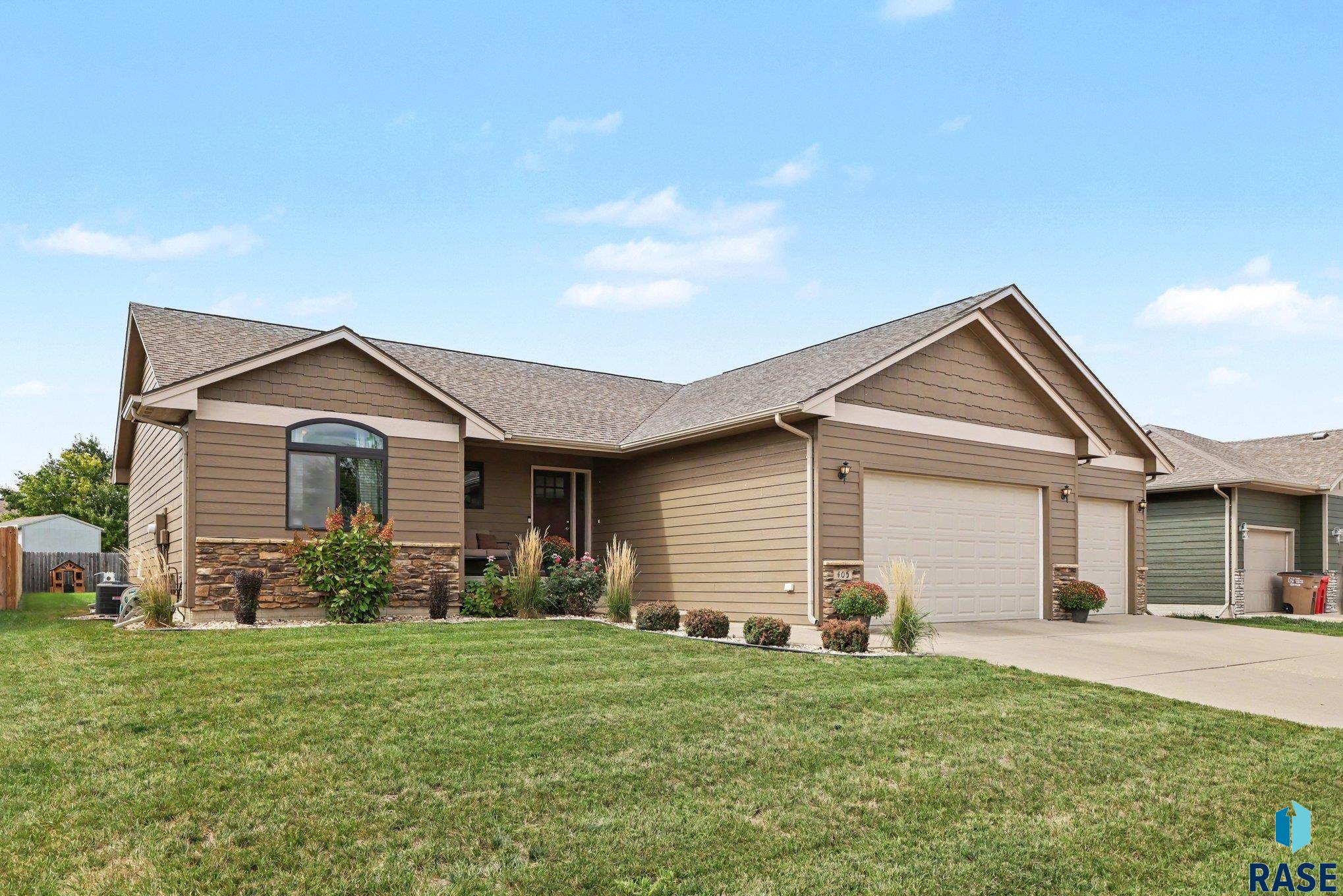 Tan single-story home with stone accents, a two-car garage, and landscaped front lawn.
