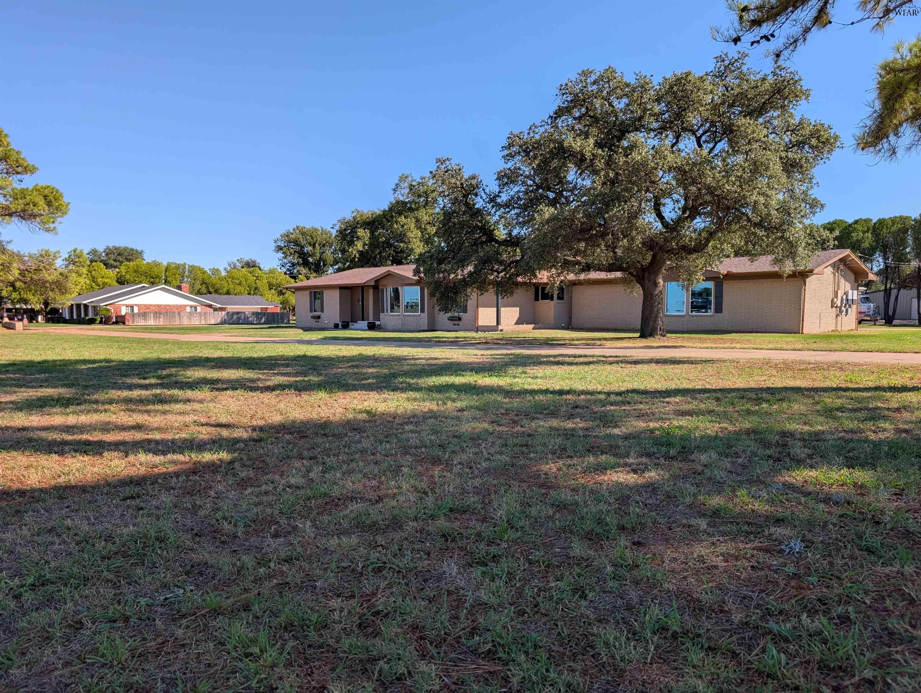 Single-story brick ranch house shaded by a large oak tree, with a broad lawn in front.