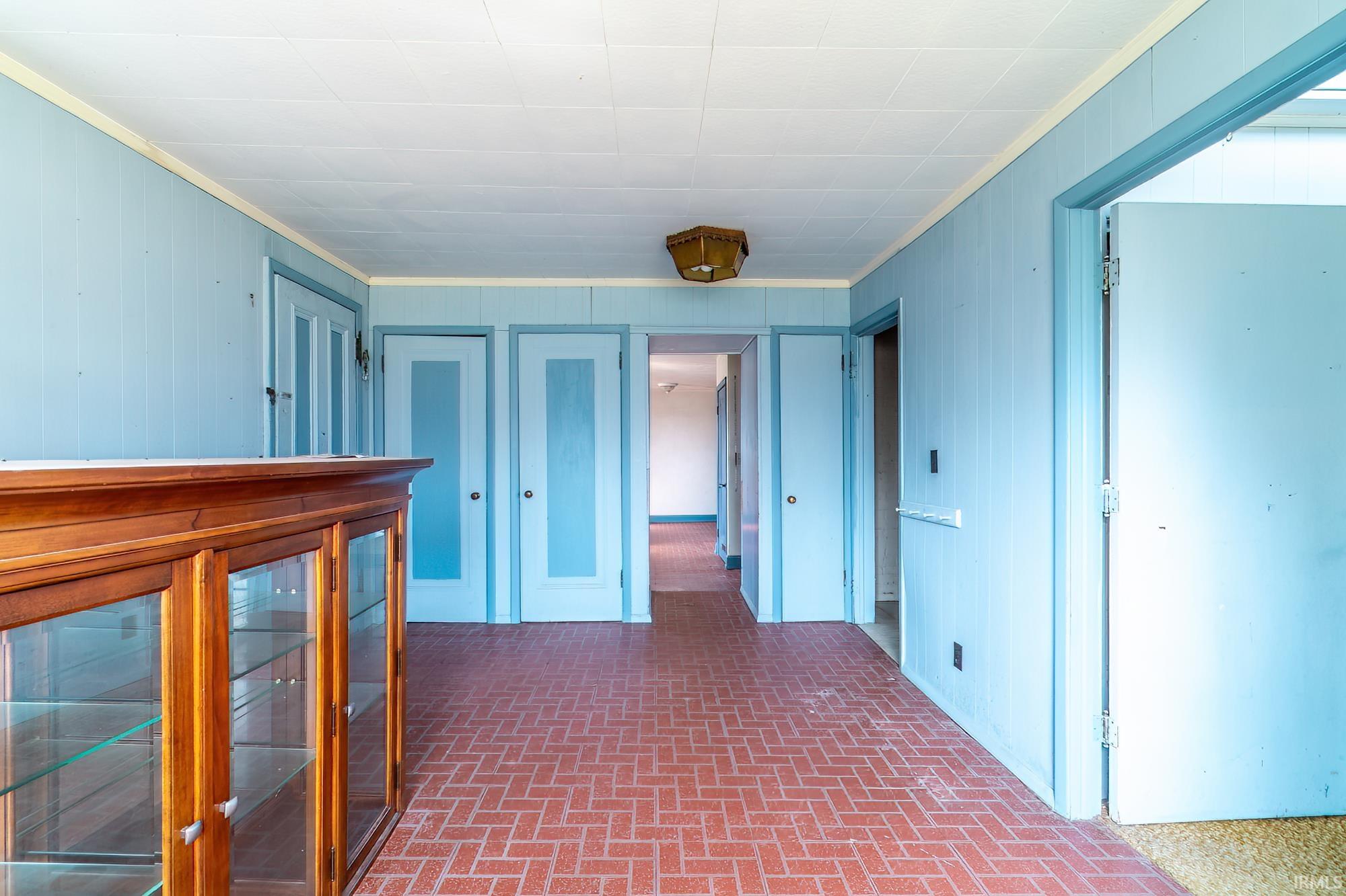 Hallway with brick patterned floors, crown molding, and wooden walls