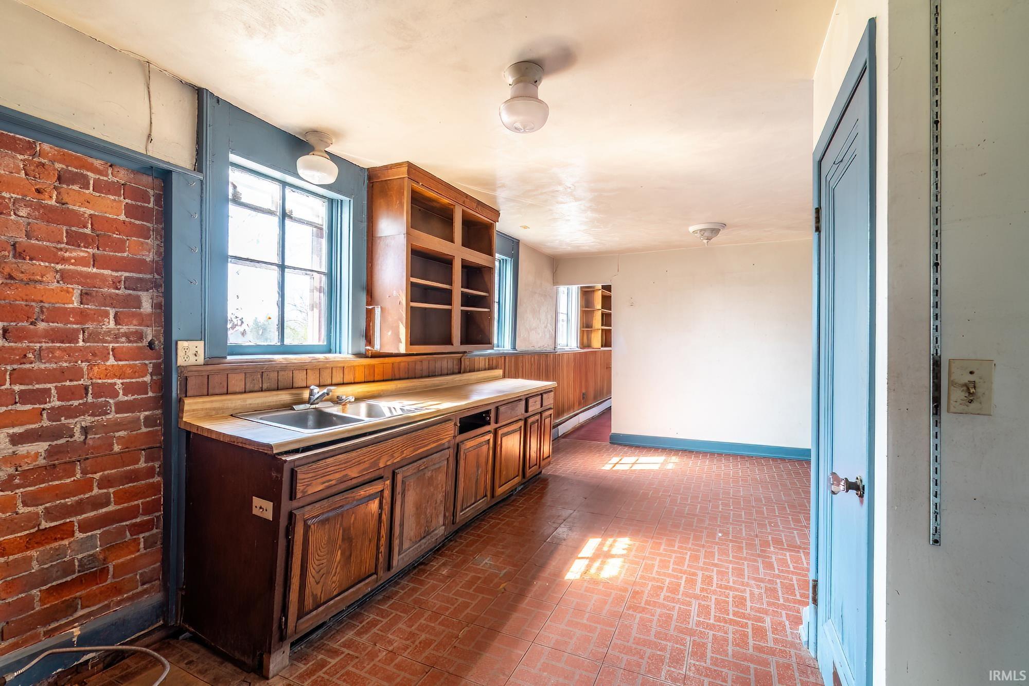 Kitchen with light countertops, a baseboard heating unit, brick patterned flooring, wood finish cabinets, and open shelves