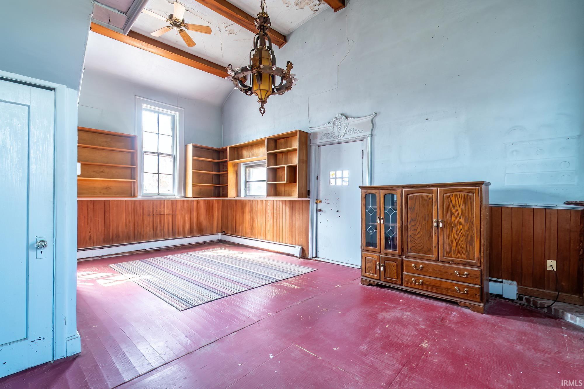 Unfurnished dining area with wood walls, ceiling fan, lofted ceiling, wainscoting, and a baseboard heating unit