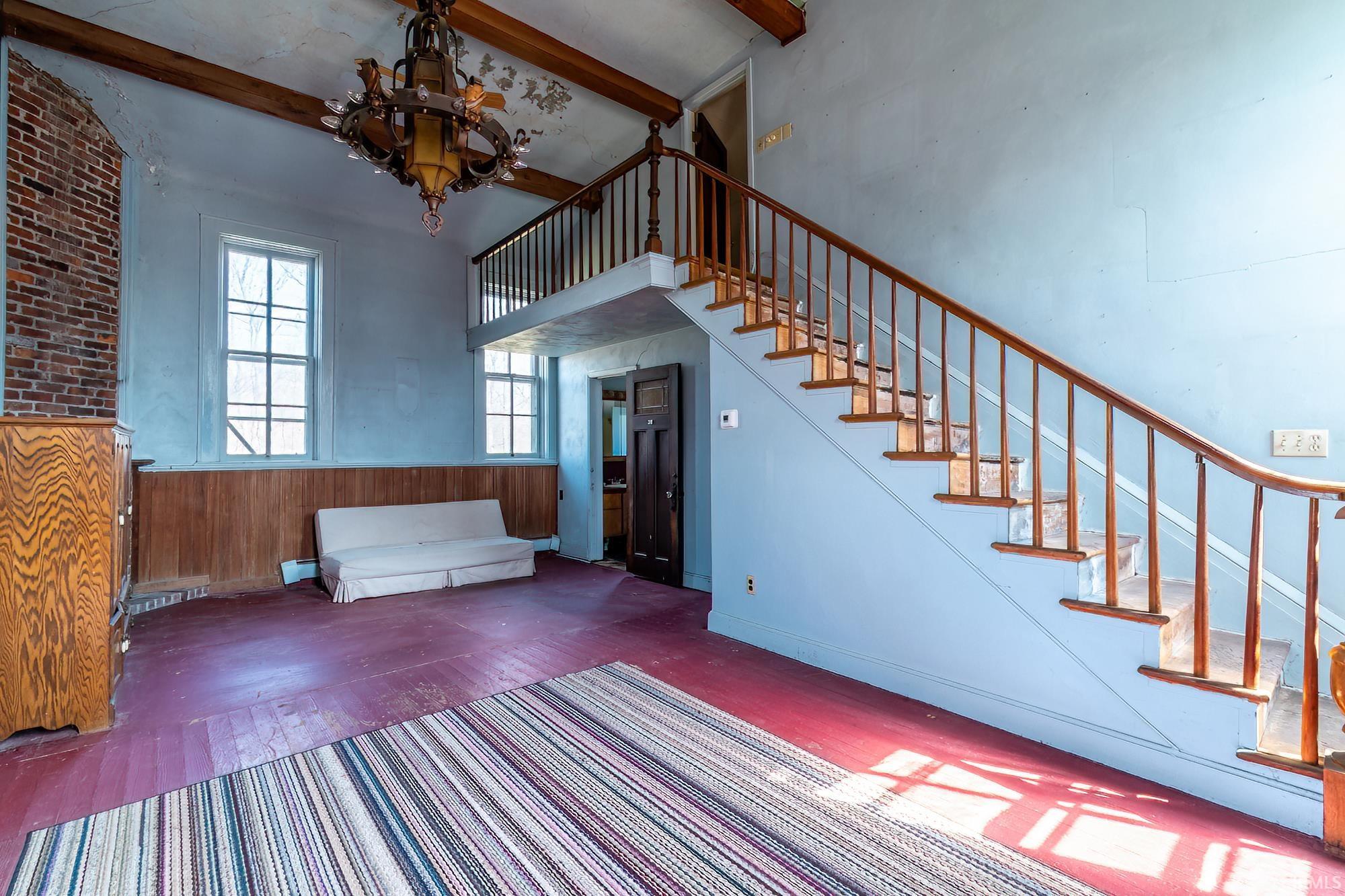 Unfurnished living room featuring wainscoting, hanging lights, wood finished floors, and wood walls