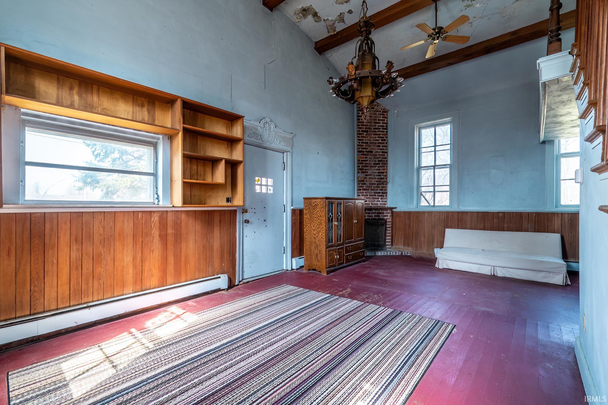 Empty room featuring ceiling fan, a baseboard heating unit, vaulted ceiling, dark wood-type flooring, and wood walls