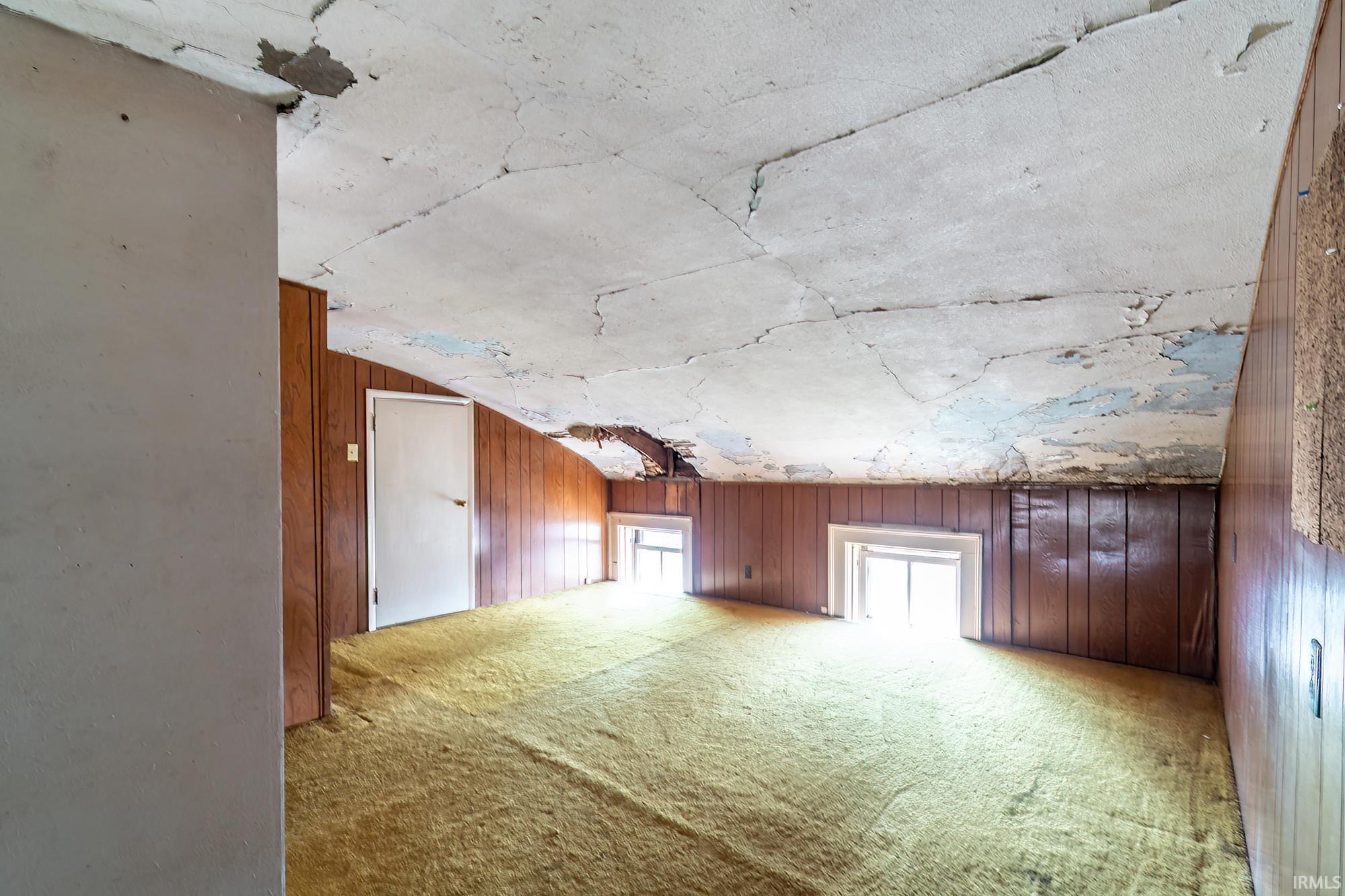 Bonus room featuring wooden walls, light colored carpet, and vaulted ceiling