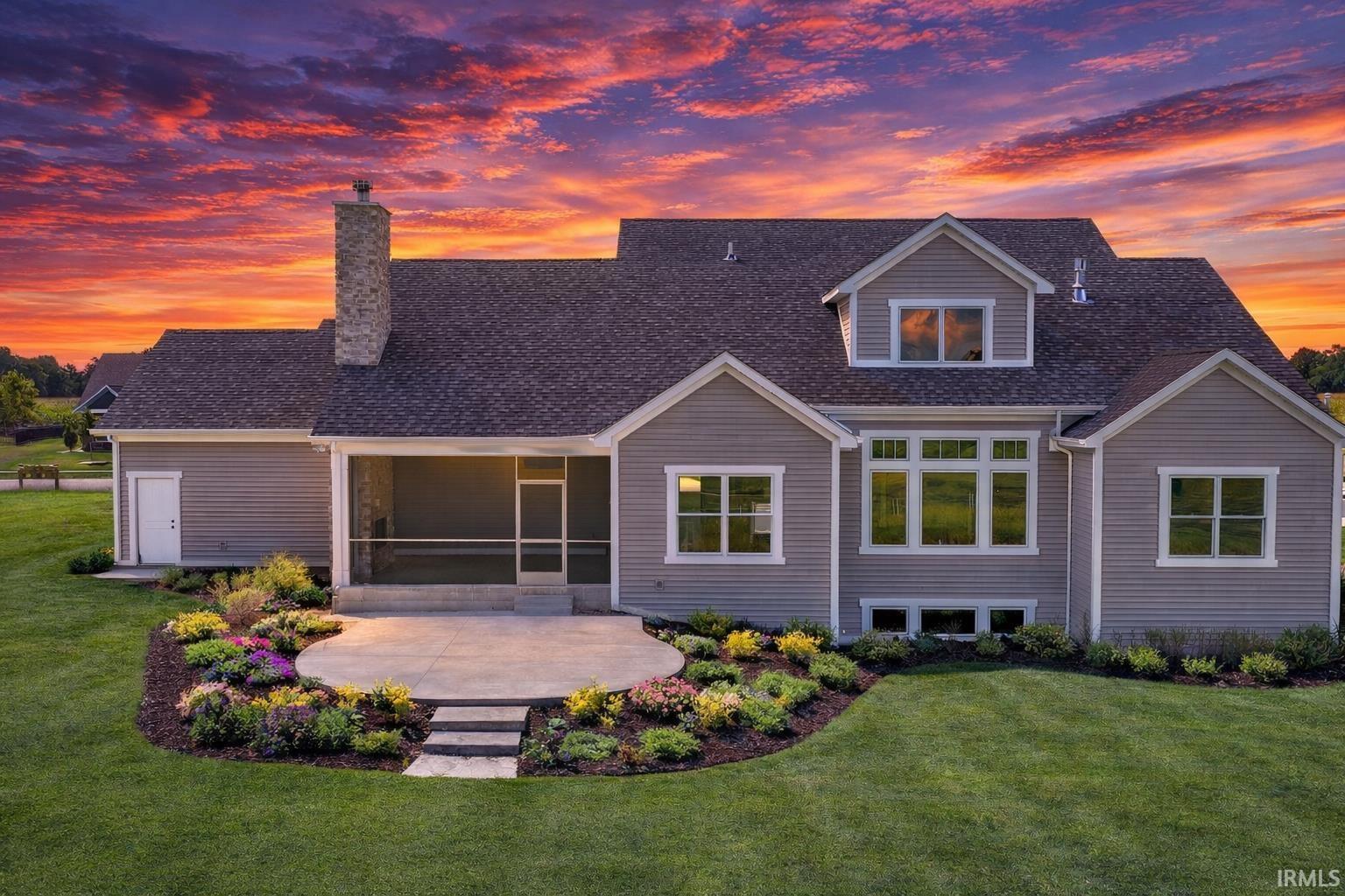 Back of house at dusk featuring a sunroom, a lawn, roof with shingles, and a chimney