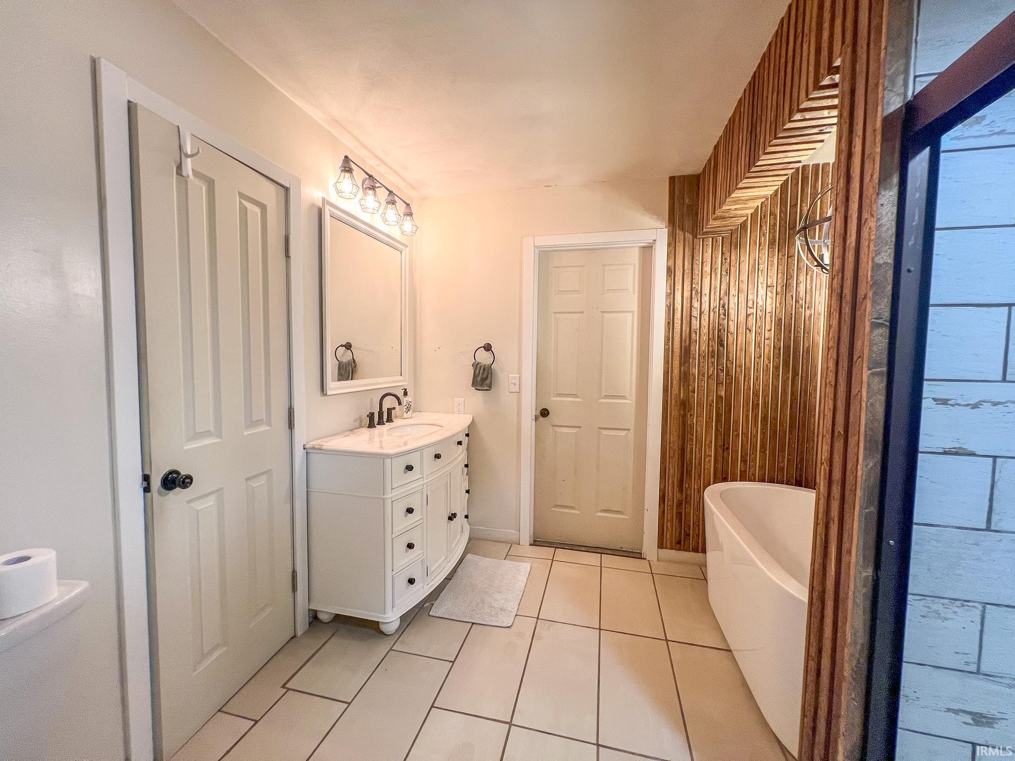 Full bathroom featuring a freestanding bath, wood walls, vanity, and light tile patterned flooring